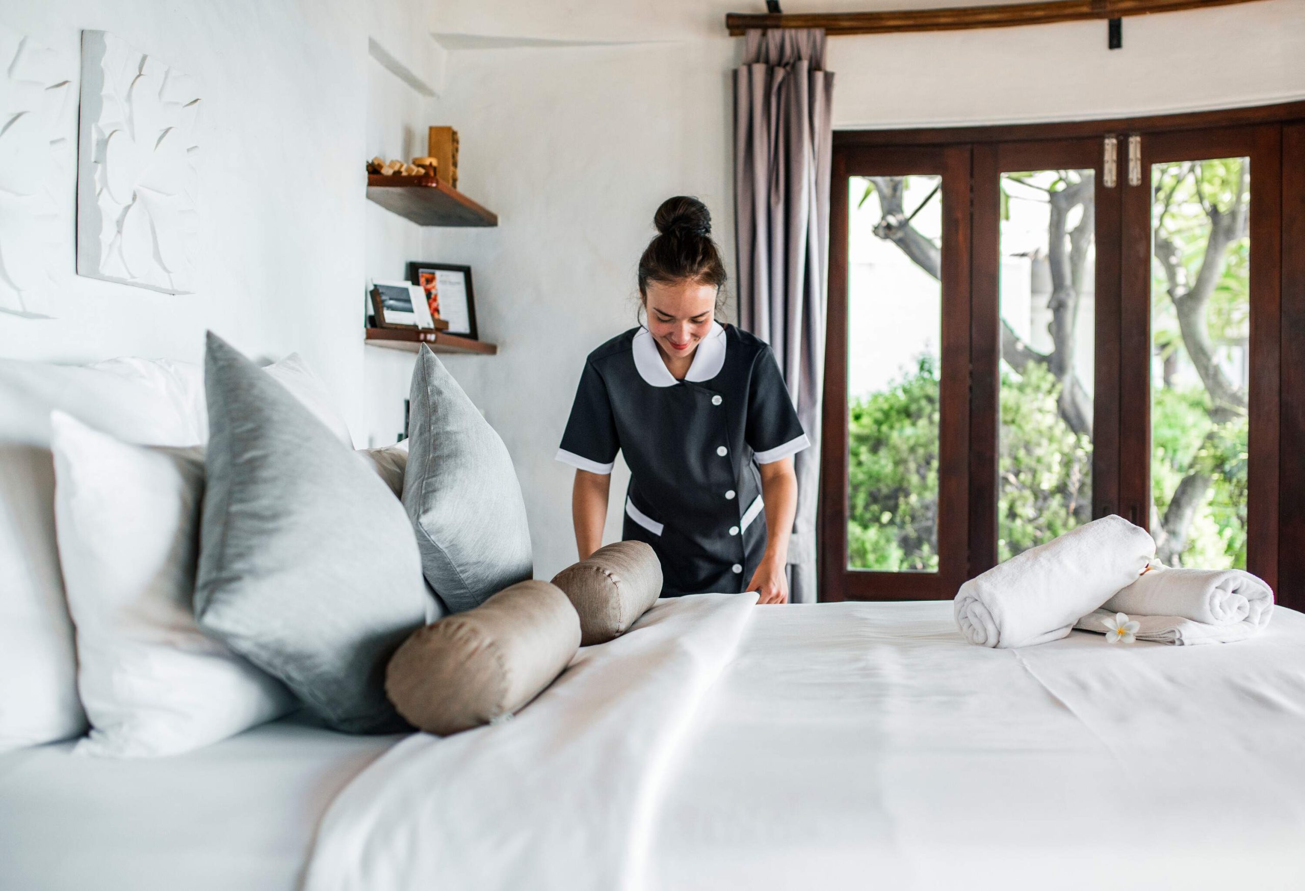 A maid in uniform with her hair in a bun making the bed.