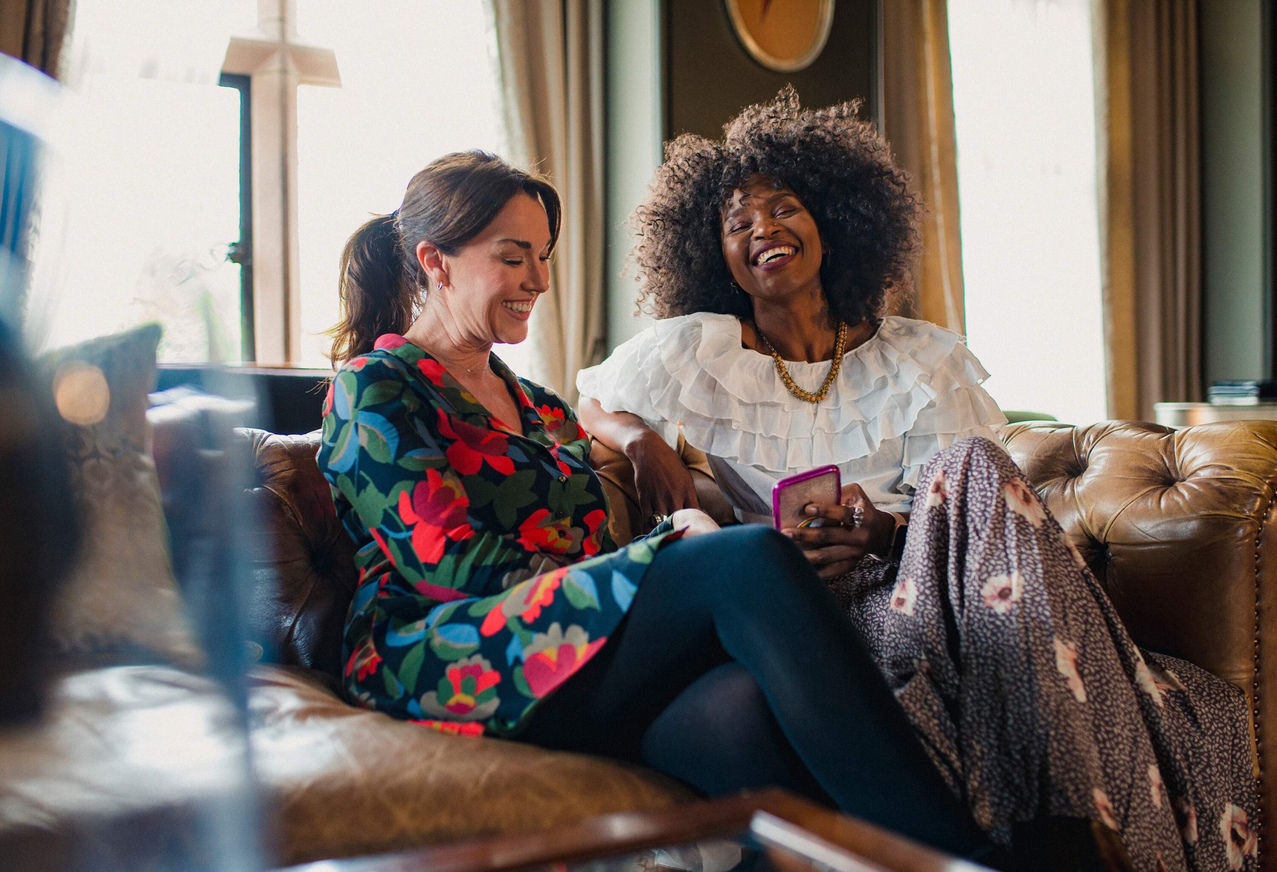 Two women sitting on a couch and laughing together.