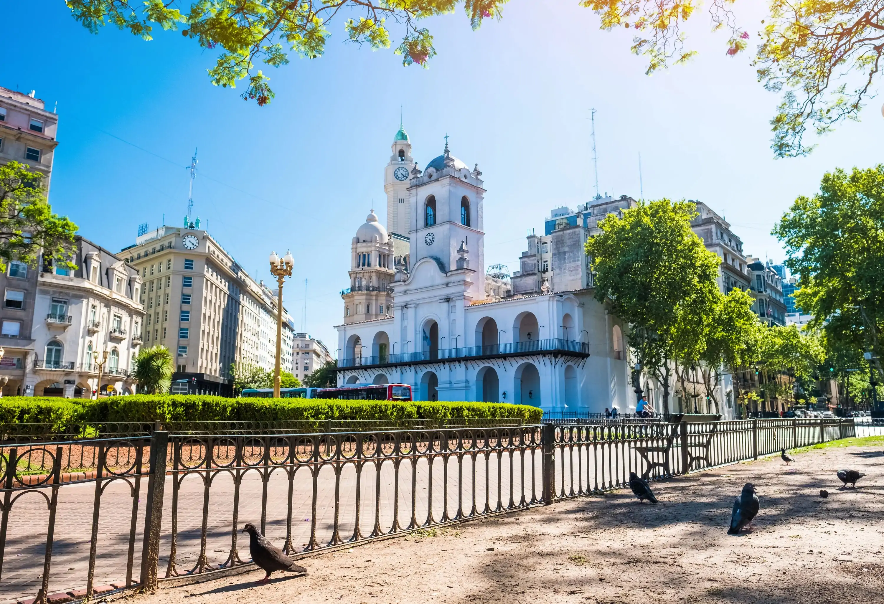 Pigeons are on the grounds adjacent to a white Baroque museum building crowned with a tower clustered with other tall structures.