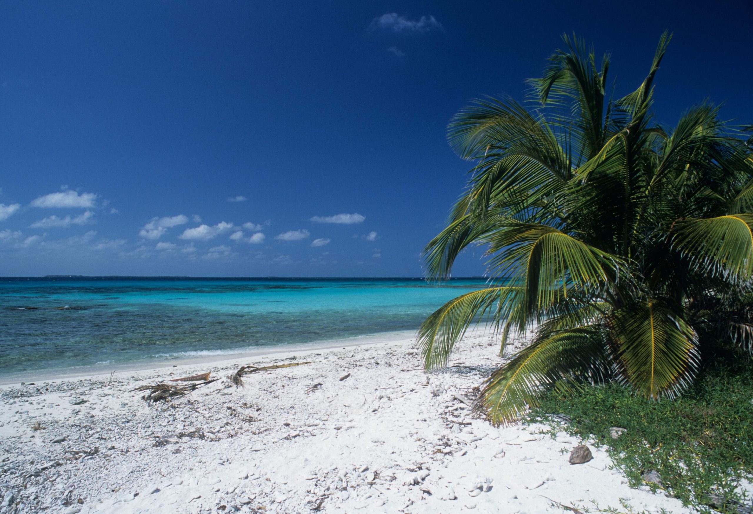 A white sand rocky shore by the tranquil turquoise sea against the cloudy blue sky.