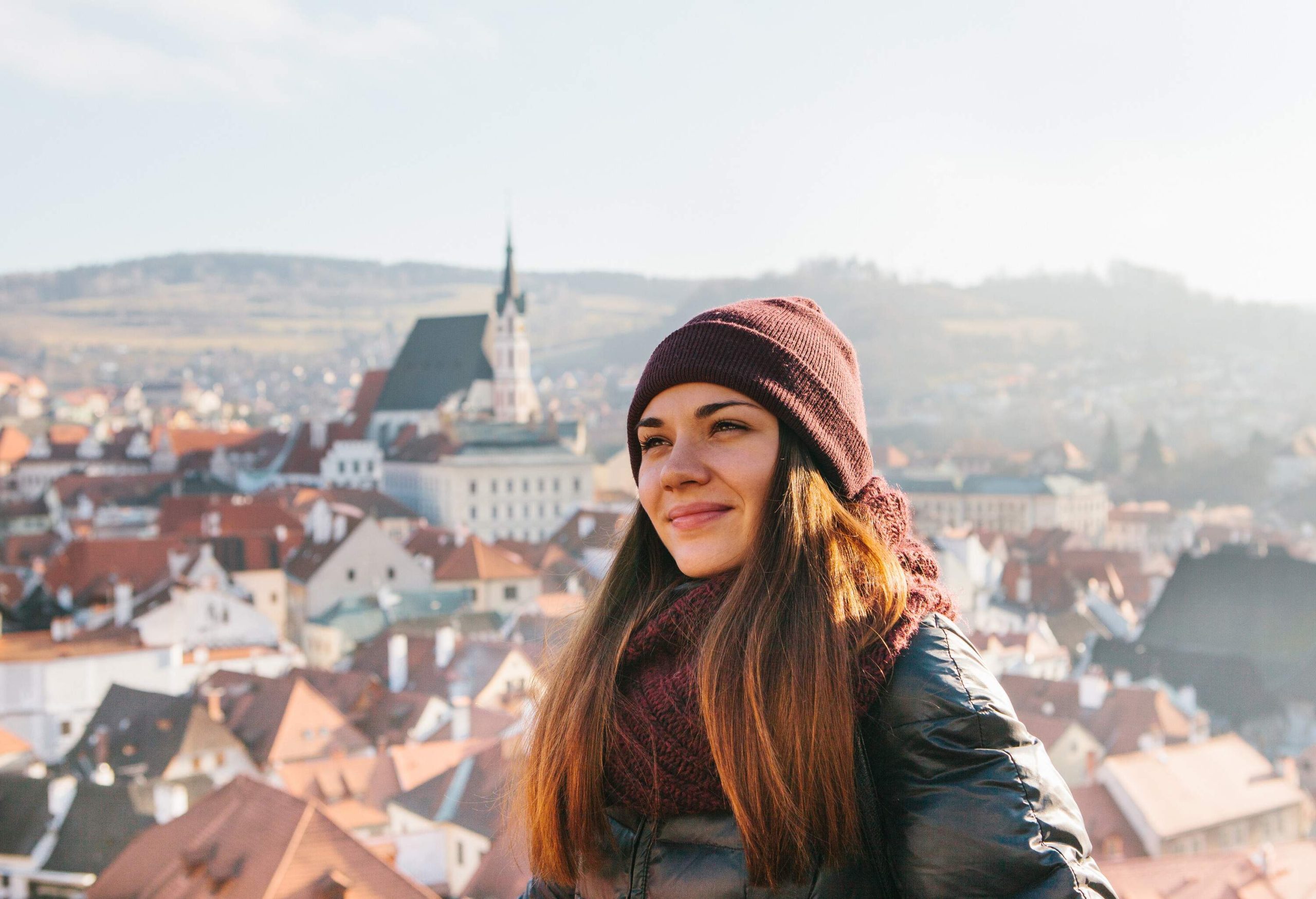A smiling brunette girl in a bonnet and winter attire against the backdrop of a townscape.