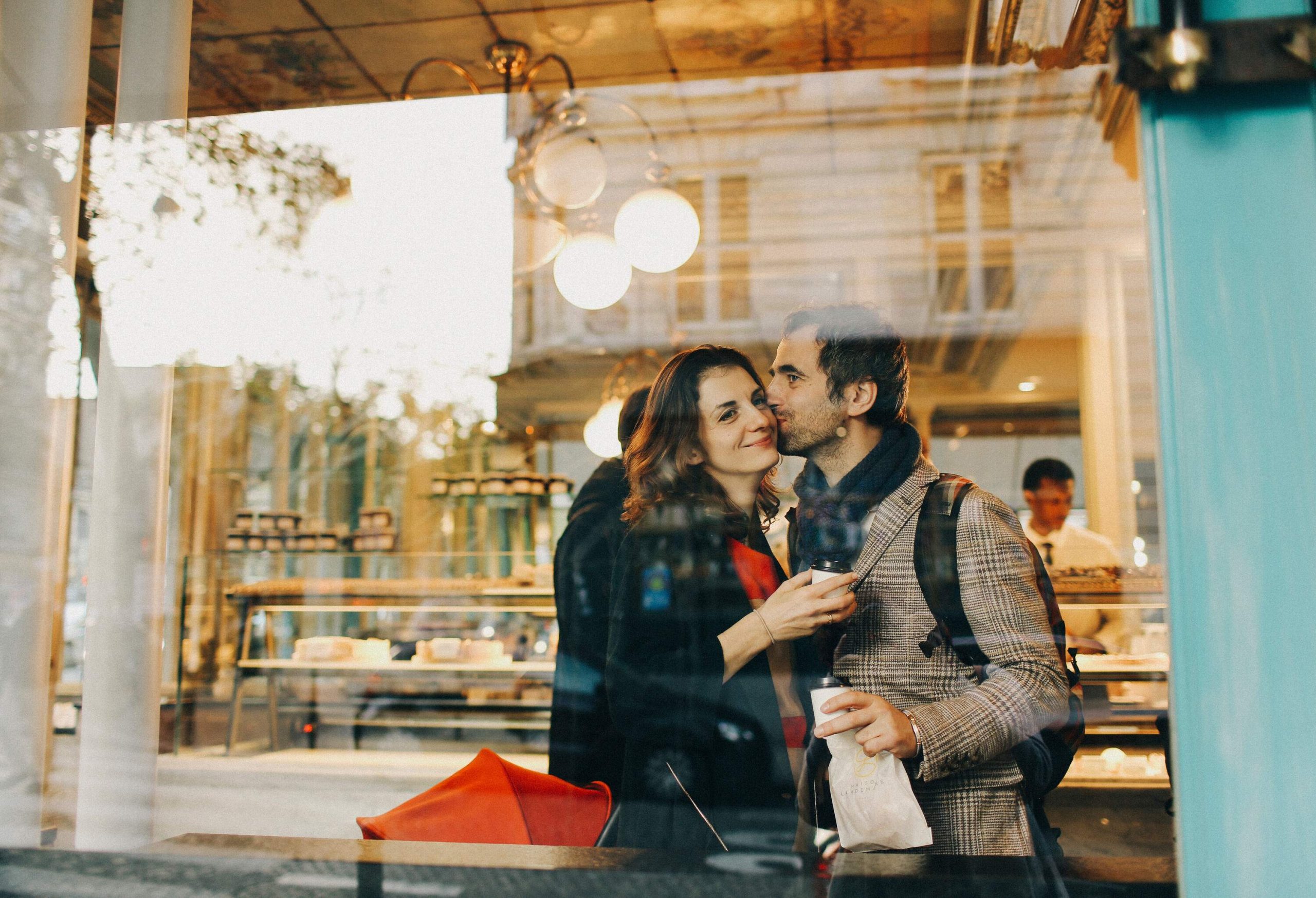 Someone kissing another person's cheek behind a glass partition in a cafe.