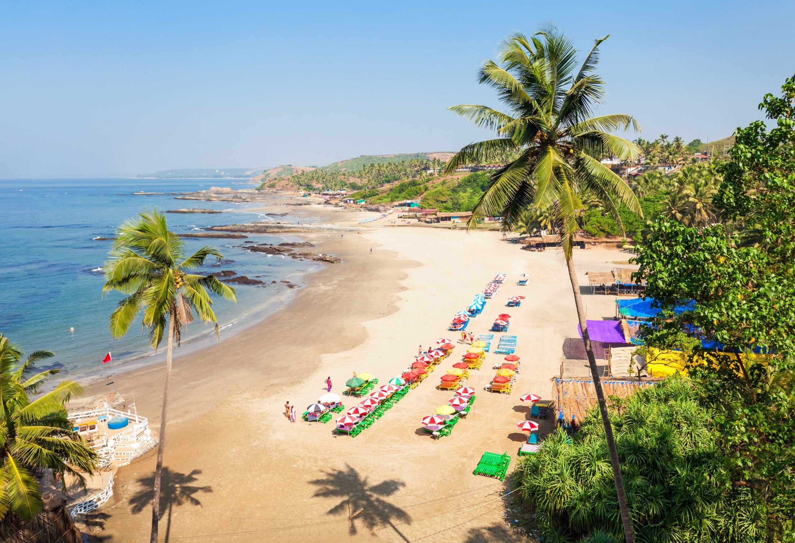 Colourful sunbeds and umbrellas lined per rows in the soft sand of the broad beach on an unclouded sky.