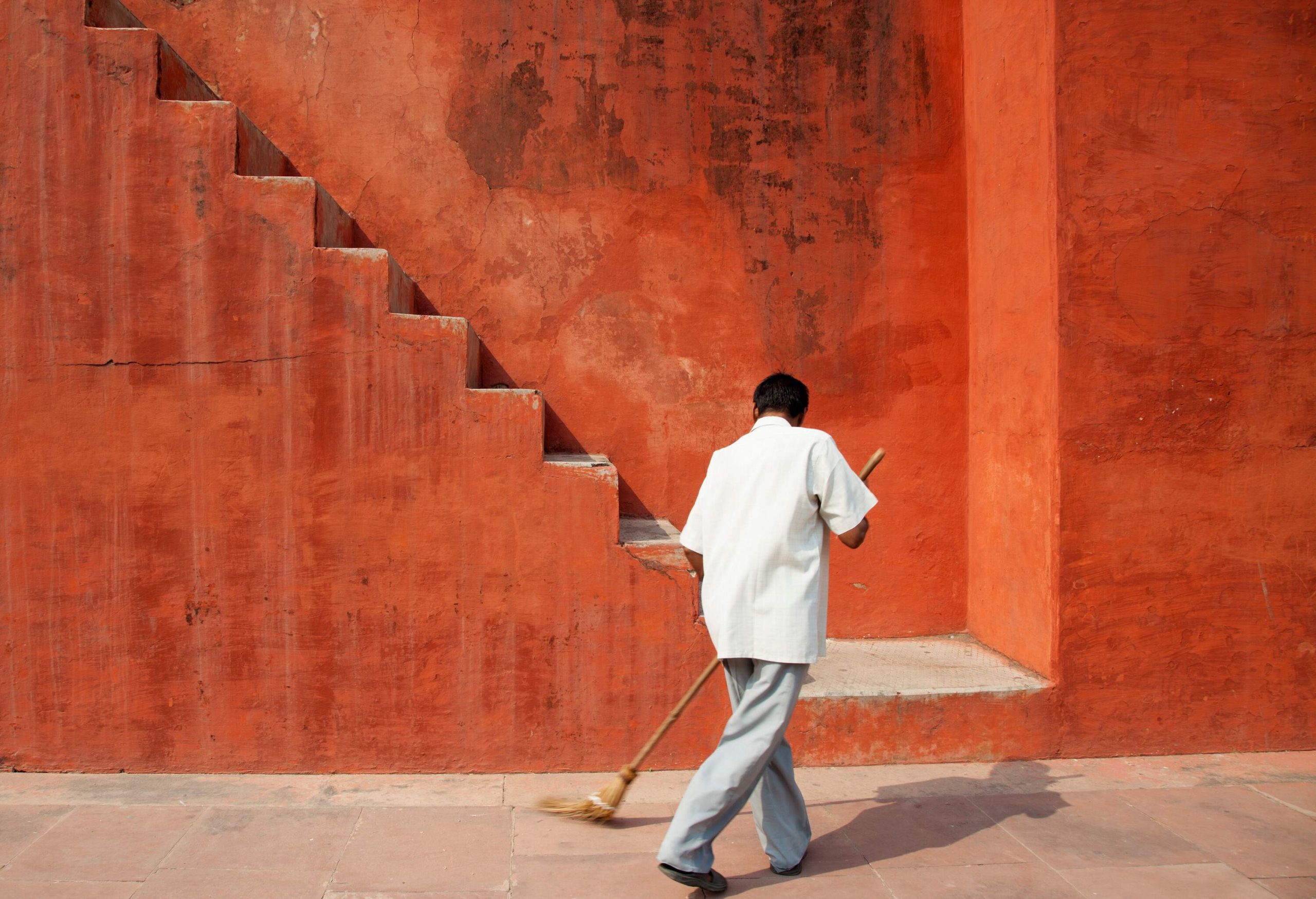 A man sweeping on a paved street by the stairs.