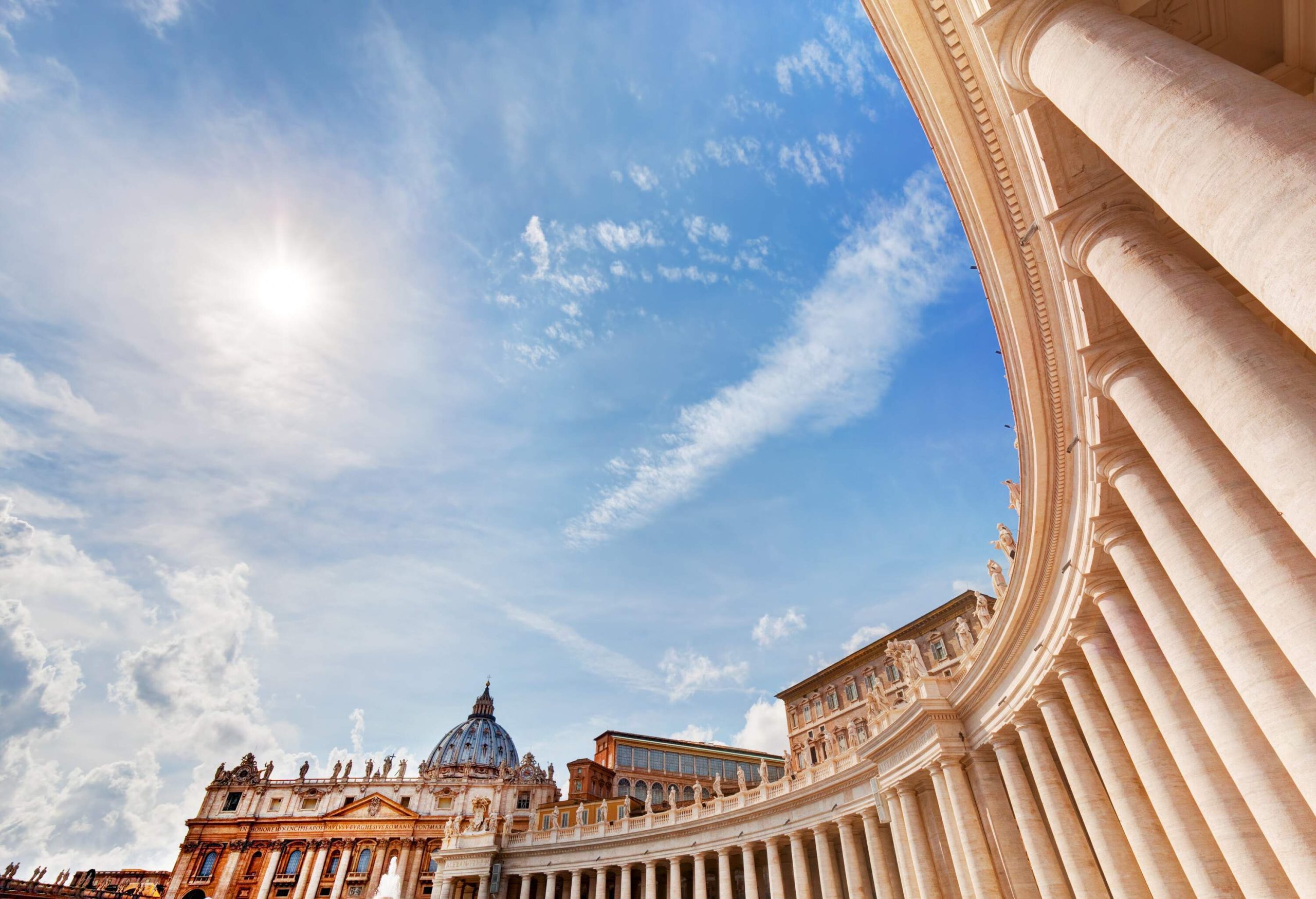 The curved colonnade and the basilica in St. Peter's Square under the bright light of the sun.