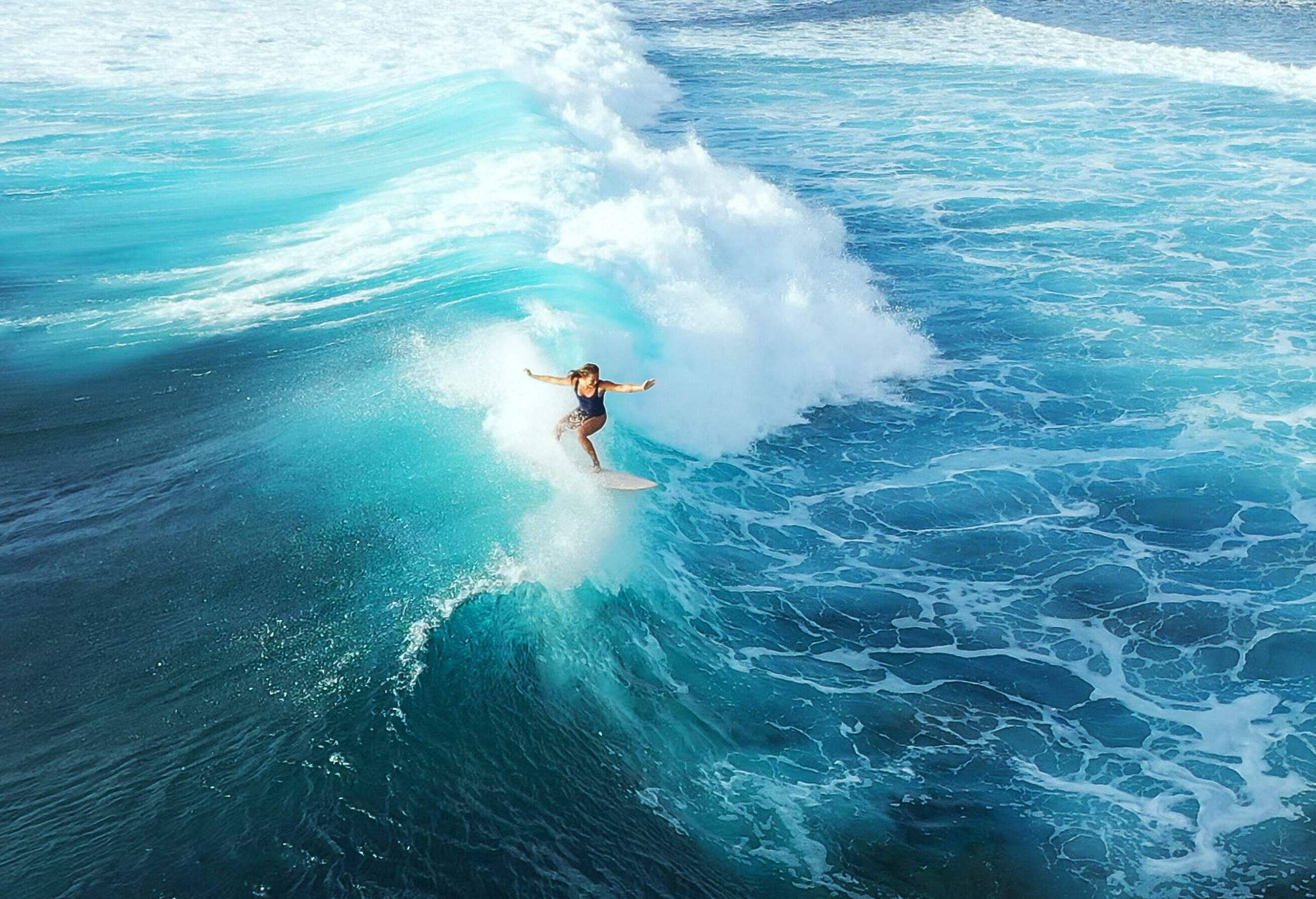 A female surfer riding the massive waves of a turquoise ocean.