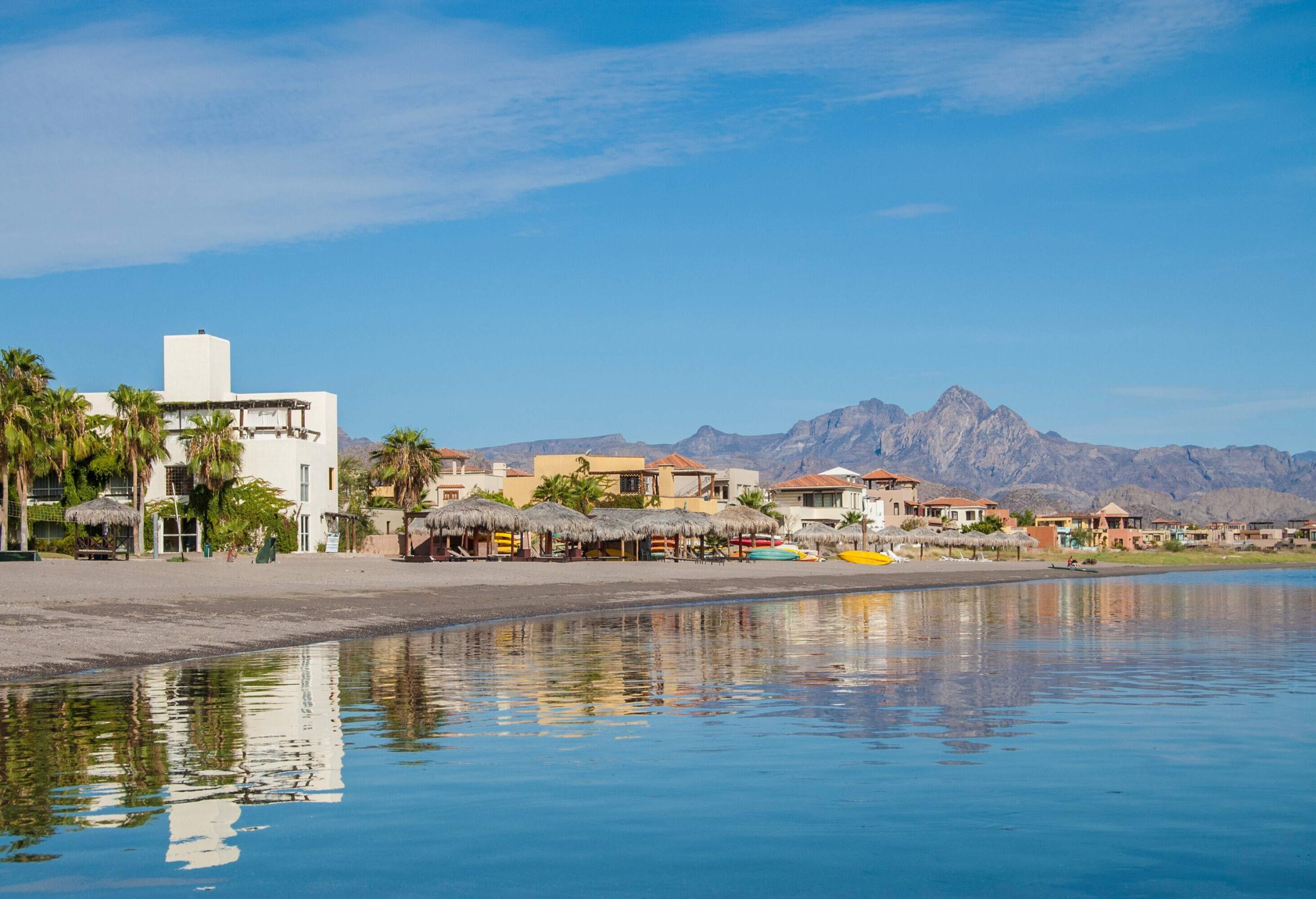 A beach with thatched cottages and beachfront properties in a coastal city.