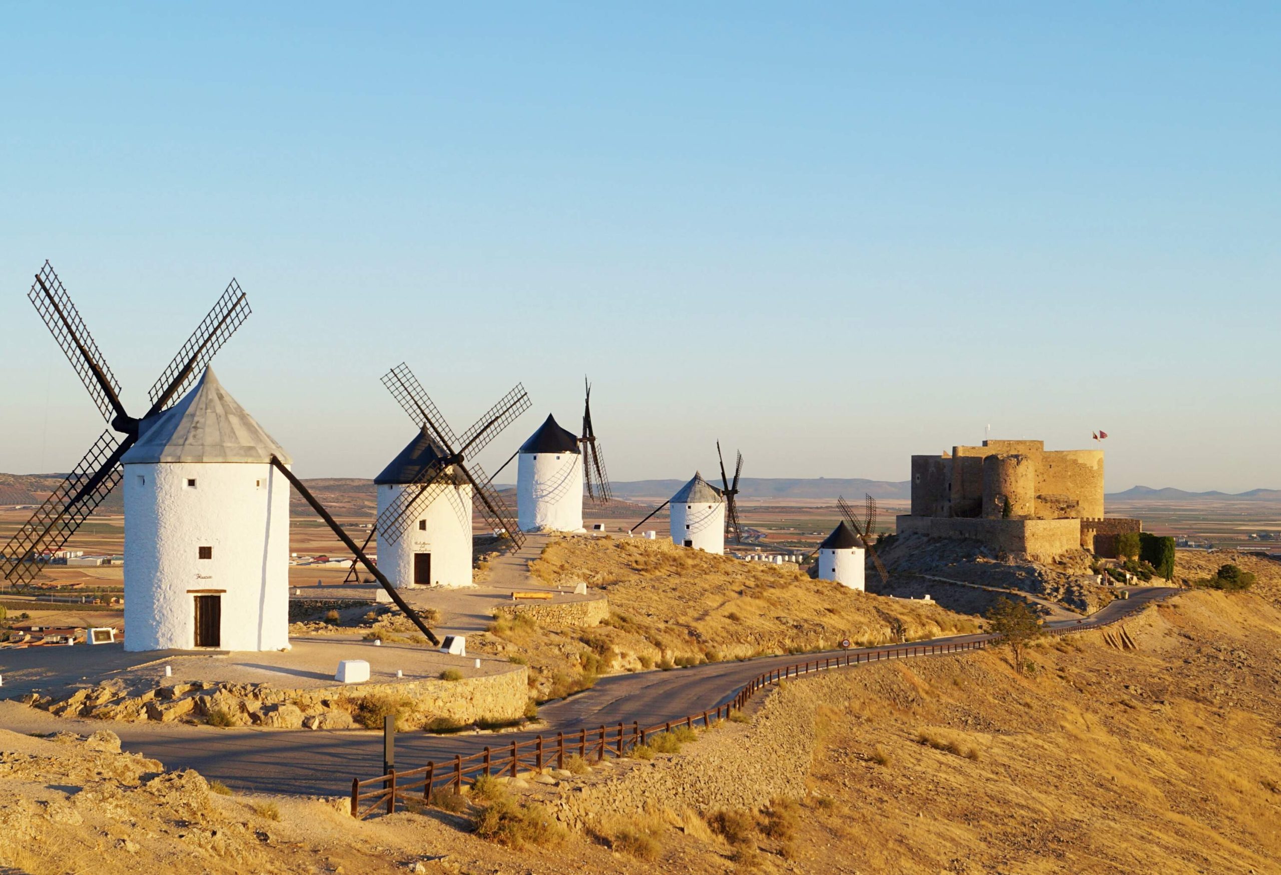 A row of windmills with white towers and conical roofs along the side of a road.