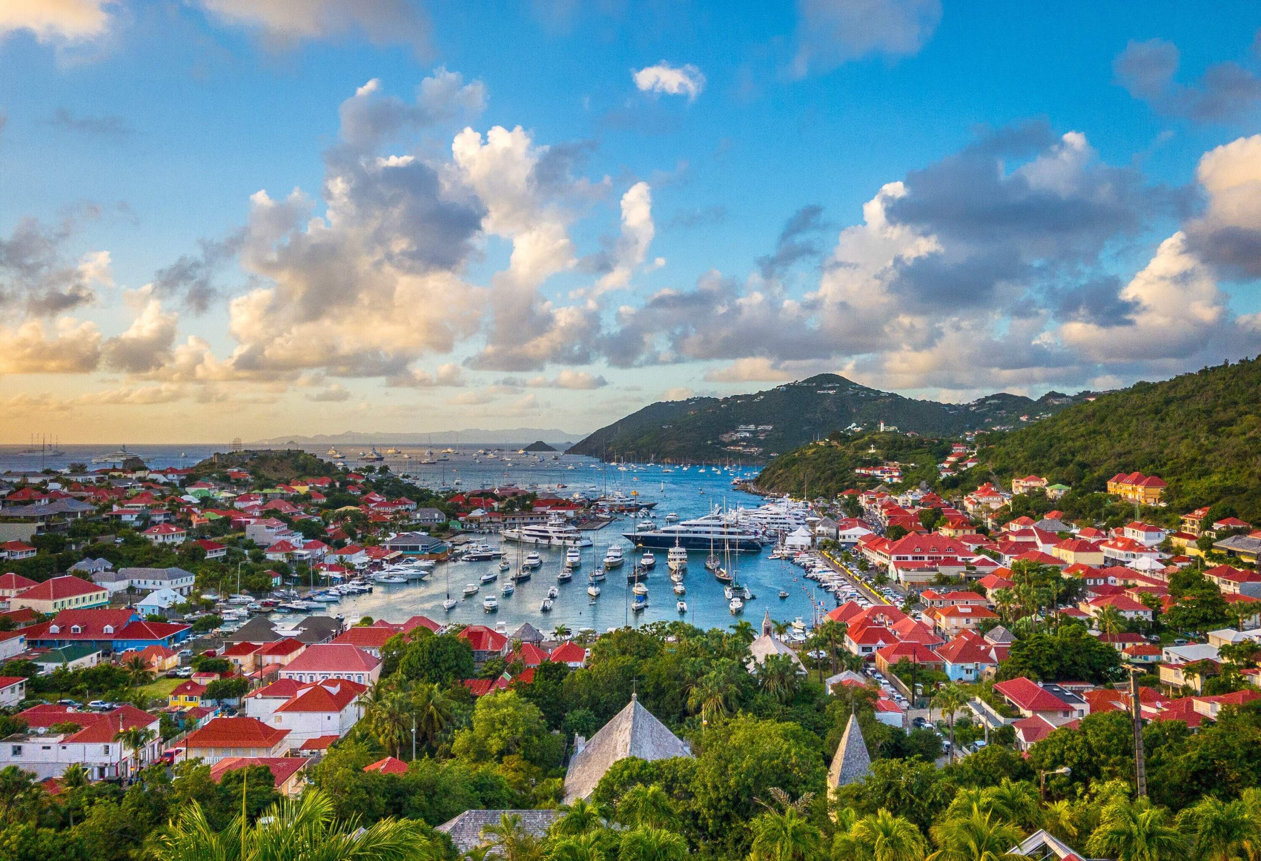 Anchored boats in a harbour surrounded by town buildings and lush foliage.