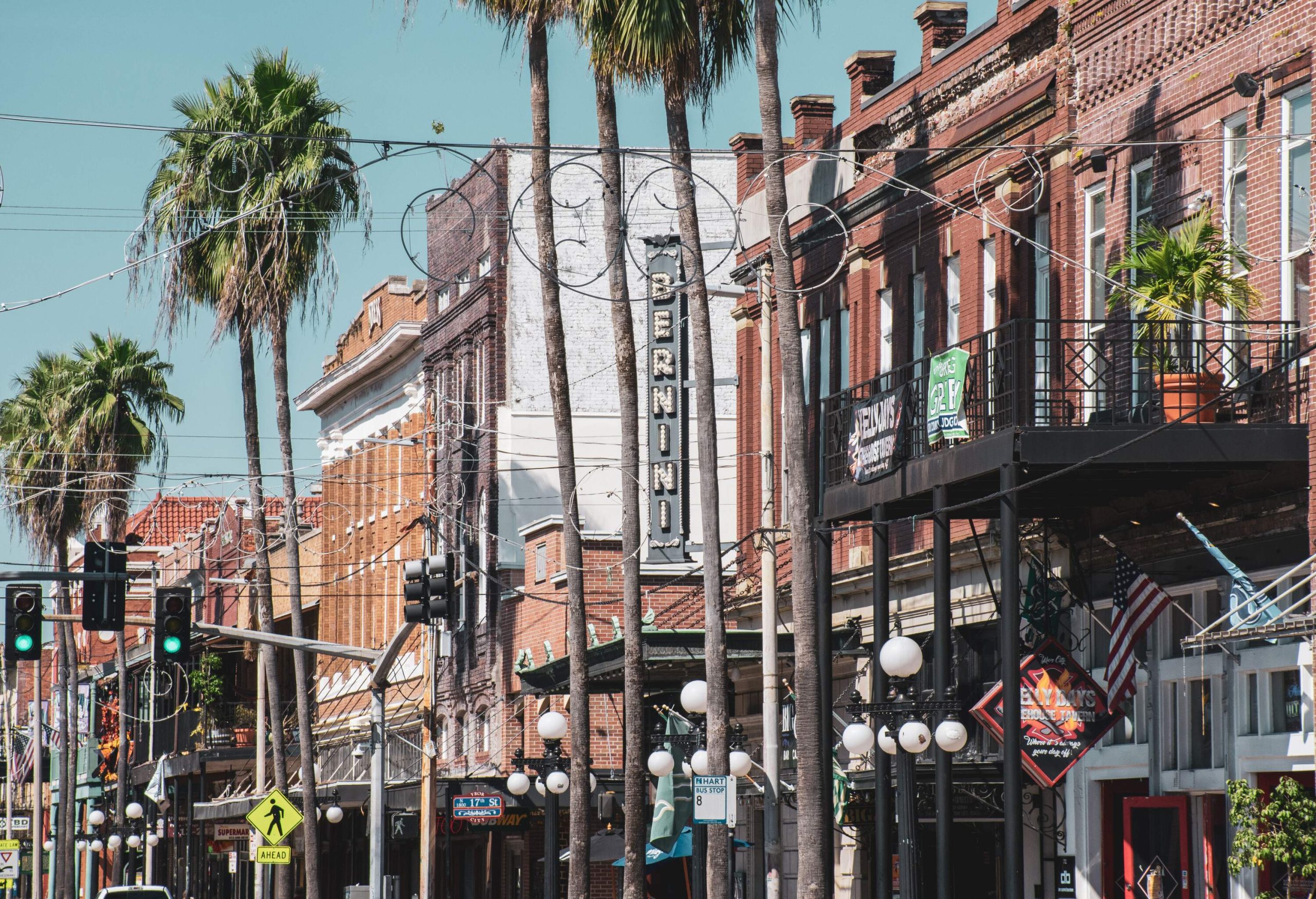 A row of old brick buildings alongside the traffic lights and tall palm trees in a historic neighborhood.