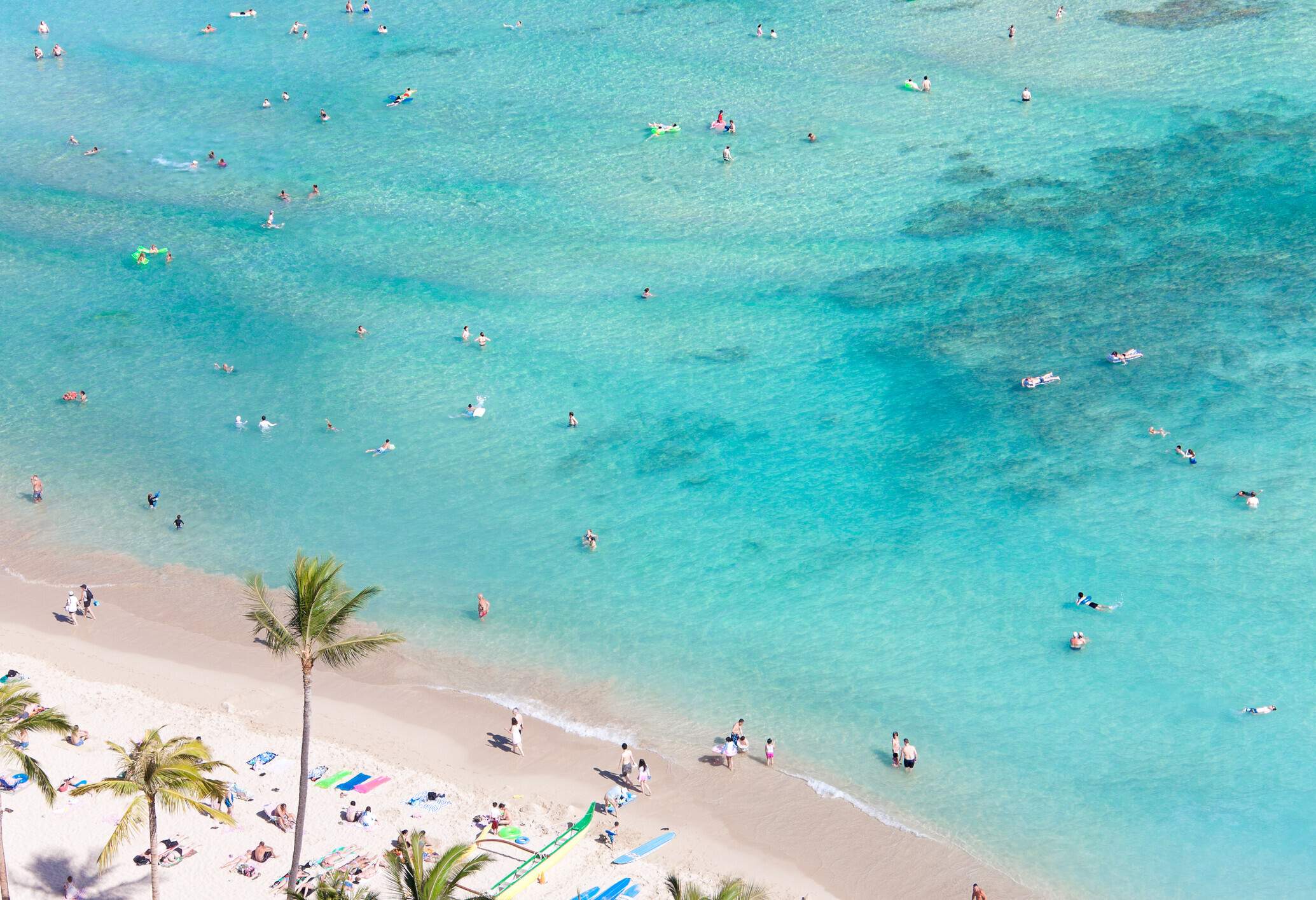 Many beachgoers swim in the shallow, turquoise, crystal-clear seawater.