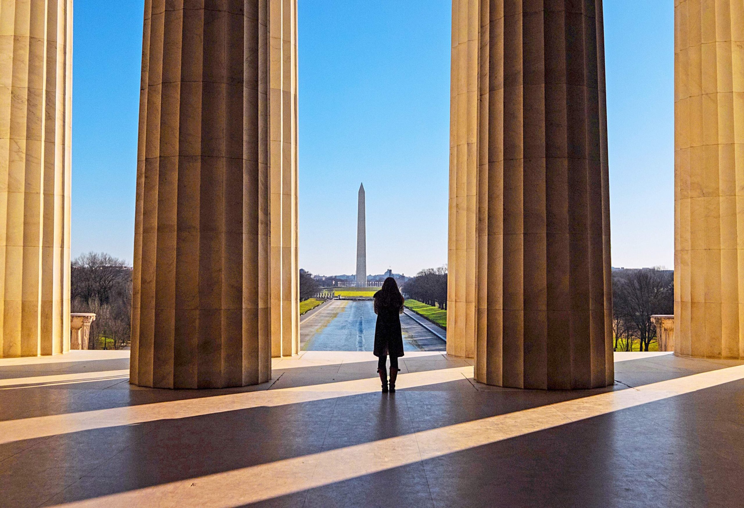 A woman standing between colossal fluted columns, with the Washington Monument in the backdrop.