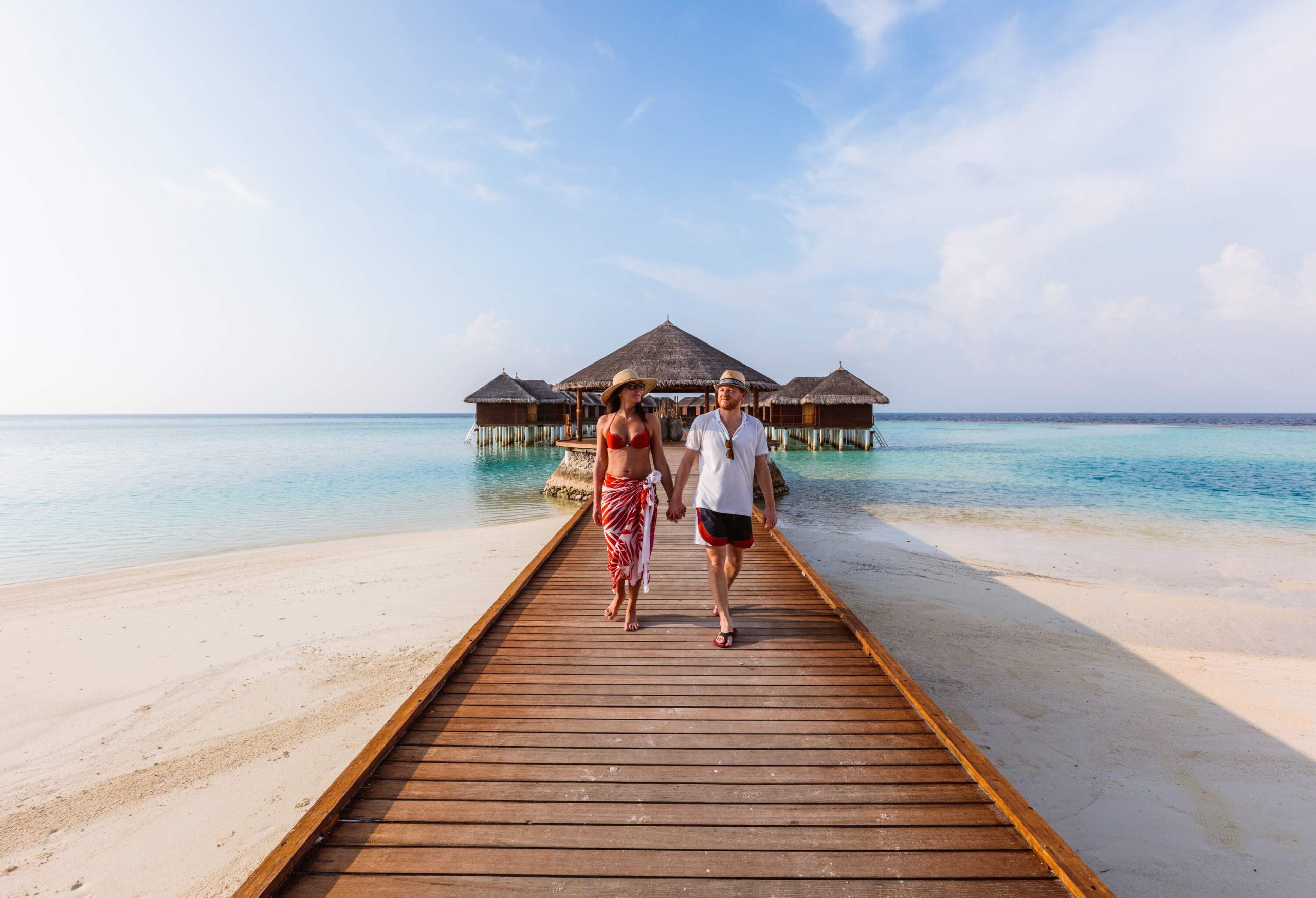 A lovely couple holding hands while walking on the boardwalk heading towards the shore.