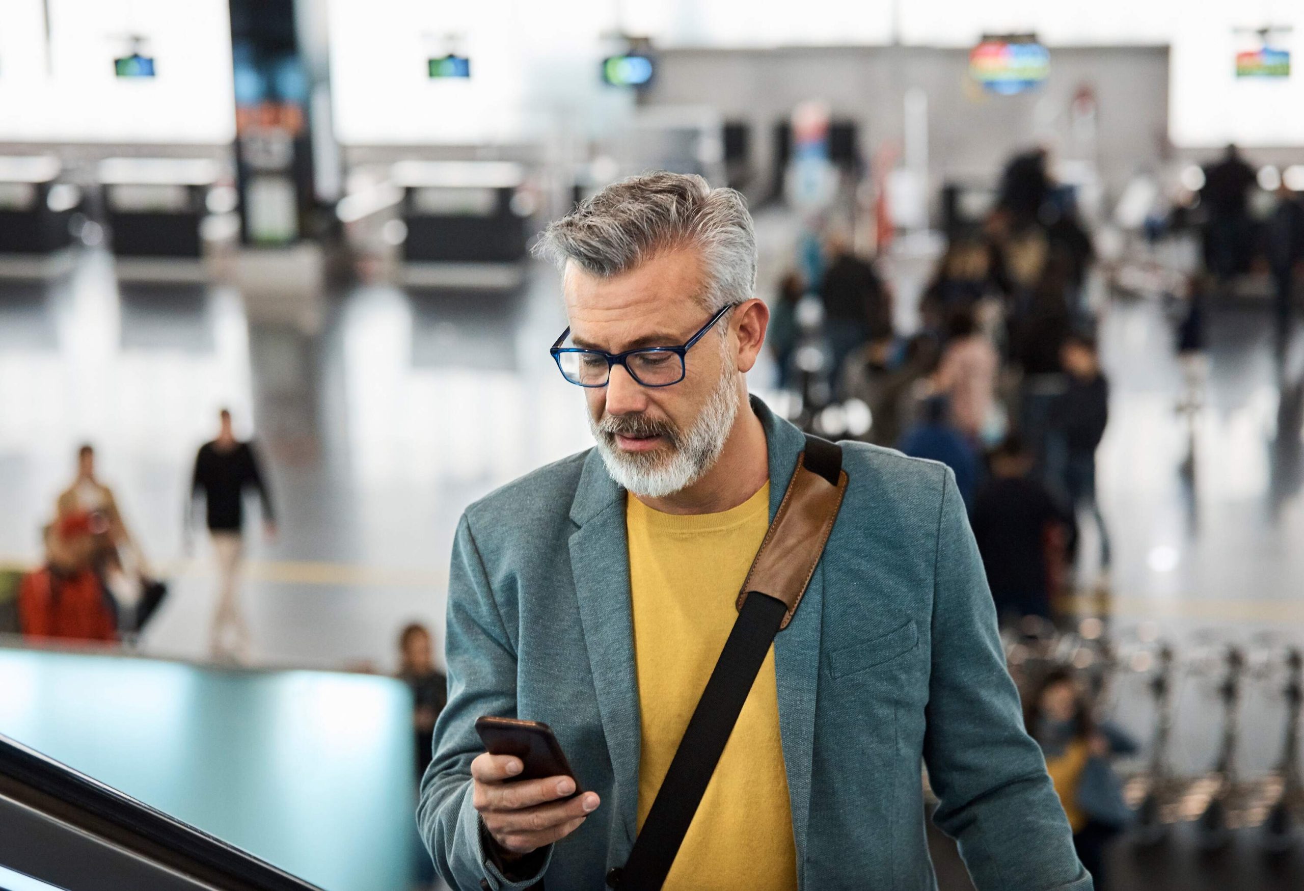 A busy man efficiently multitasks, absorbed in his smartphone as he stands on a moving escalator.