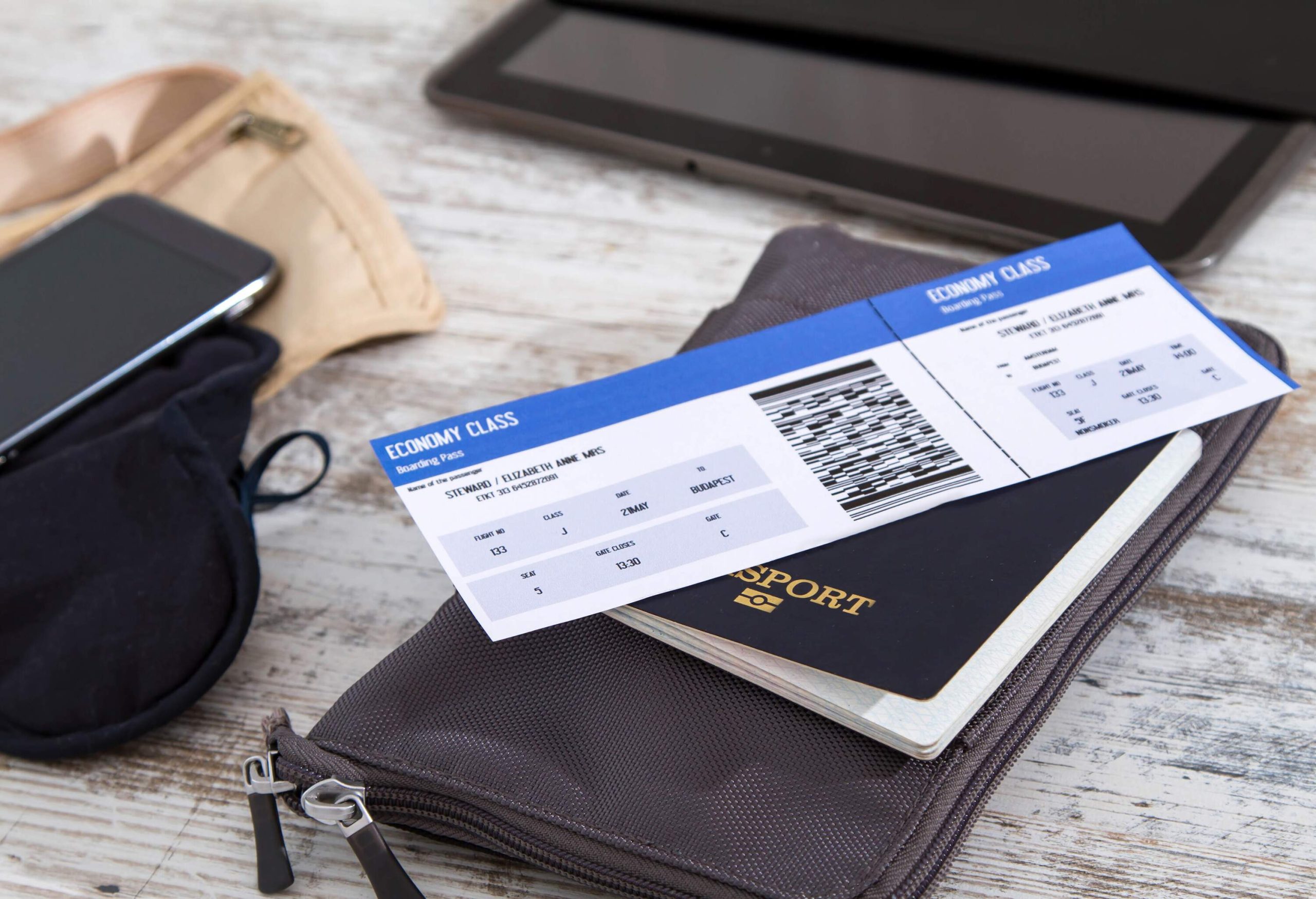 An airline ticket, passport, and electronics are arranged neatly on a surface, ready for travel.