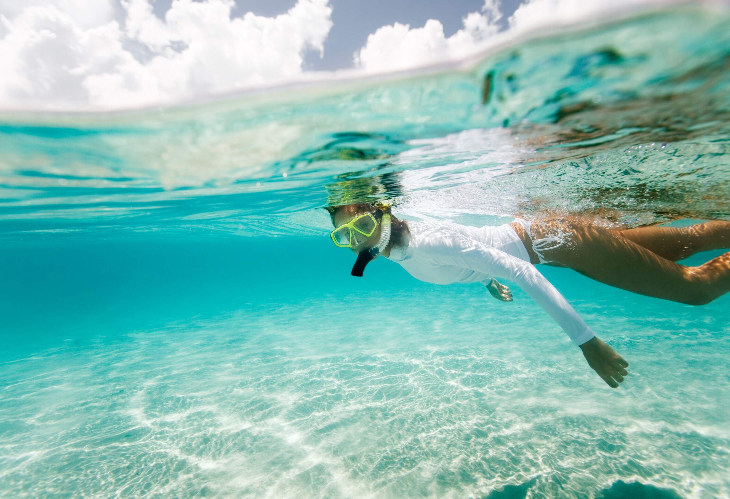 A woman in a white rash guard snorkels in a pristine ocean.