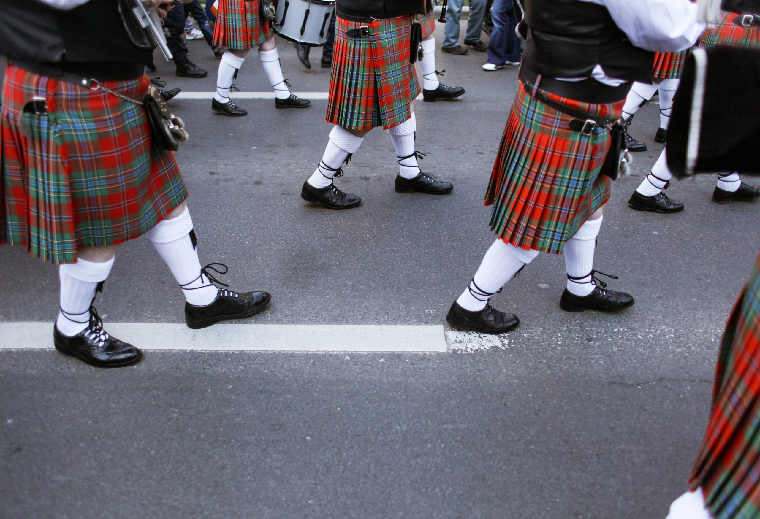 A parade of people on the street dressed in kilts.