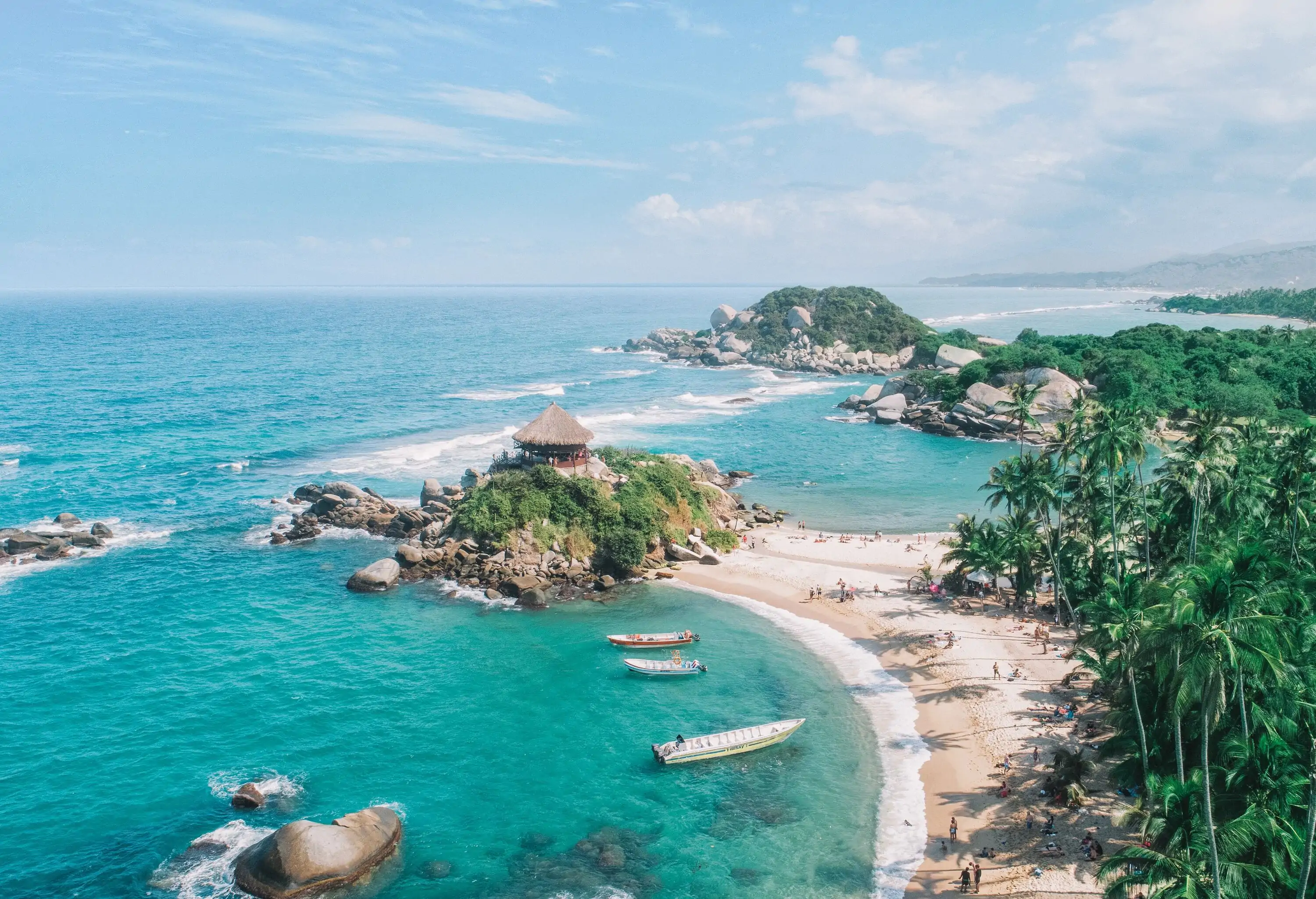 A thatched hut crowned on a rocky outcrop emerged on the turquoise seawater alongside tourists having fun at the sandy beach.