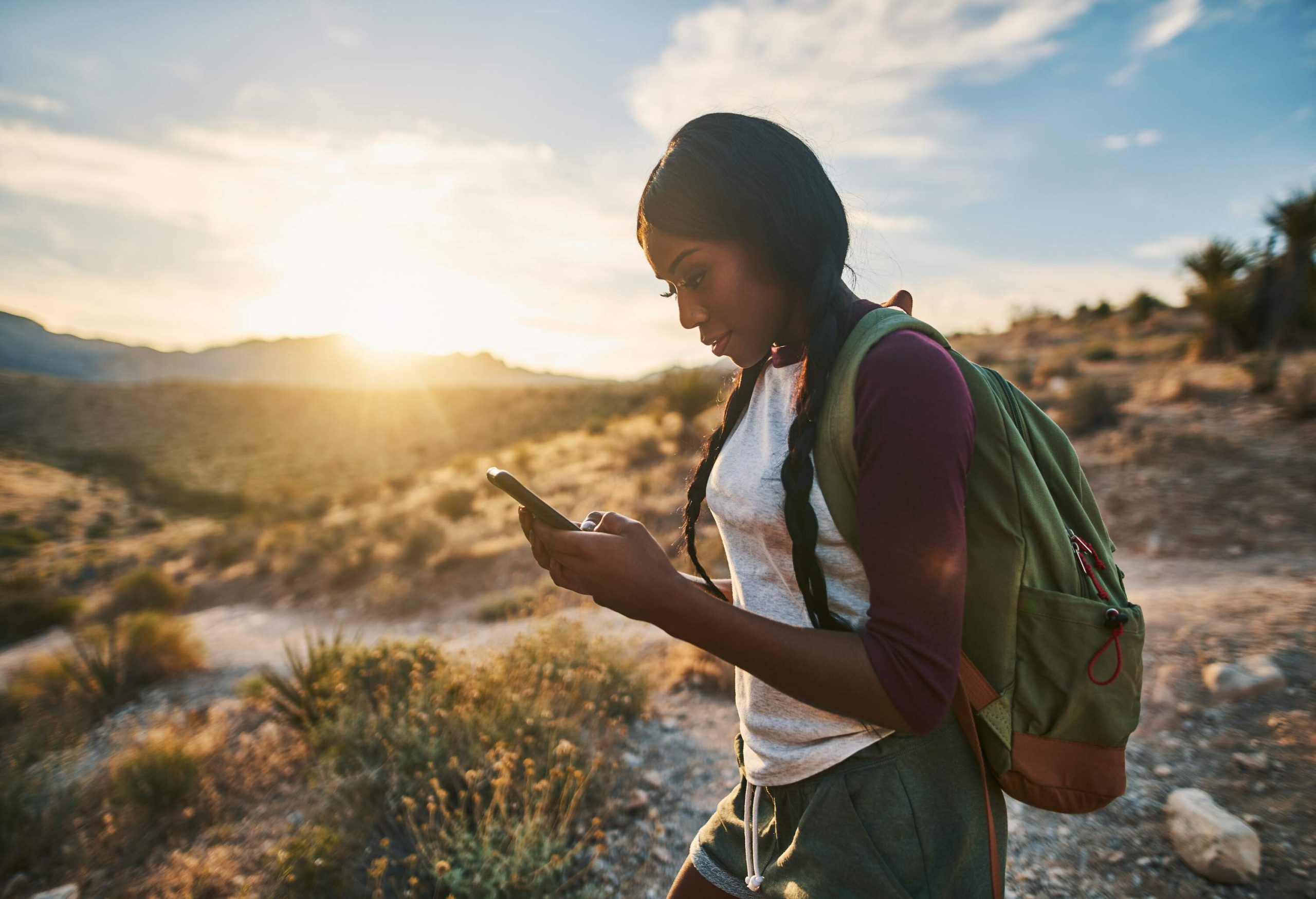 A woman with a green backpack looking at her mobile phone.