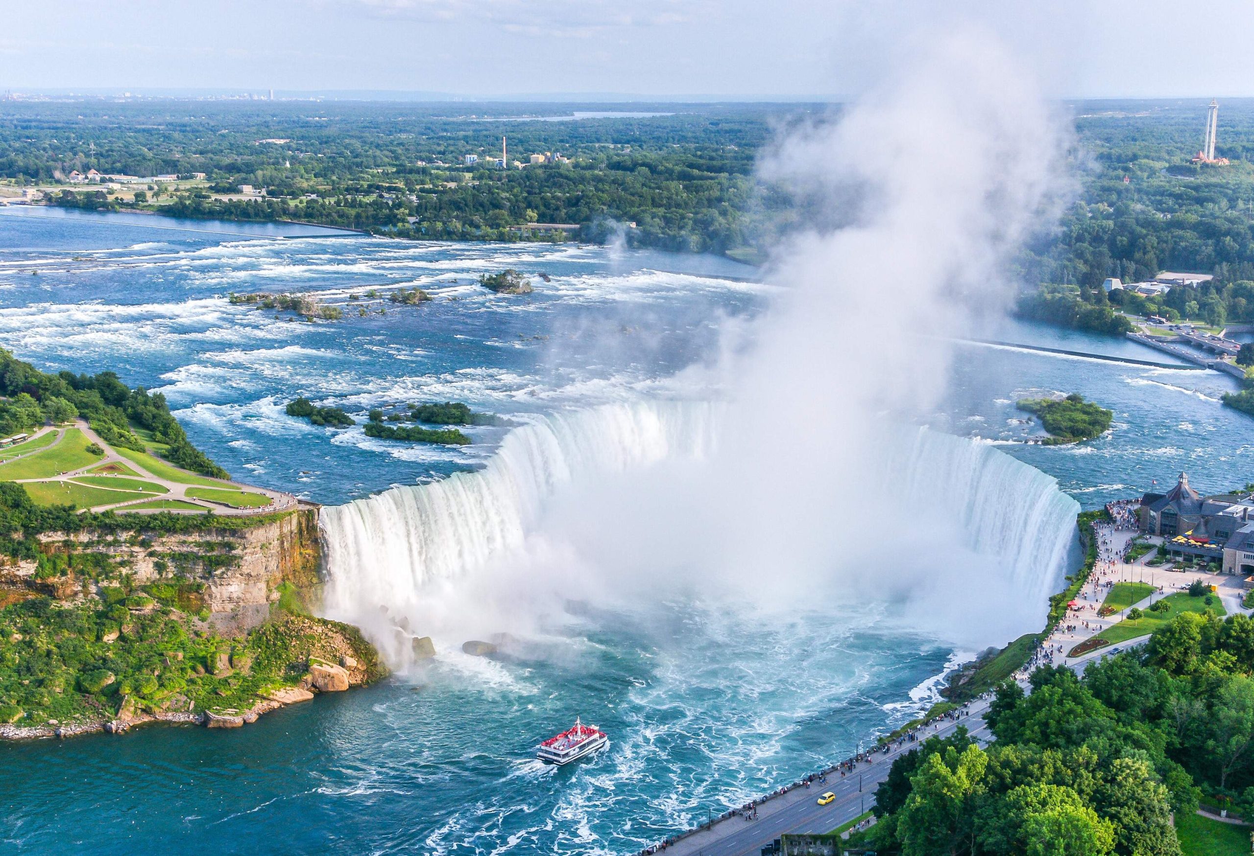 The jaw-dropping spectacular Horseshoe Falls cascade into the cliffs with a red tourist boat traversing the gushing river.