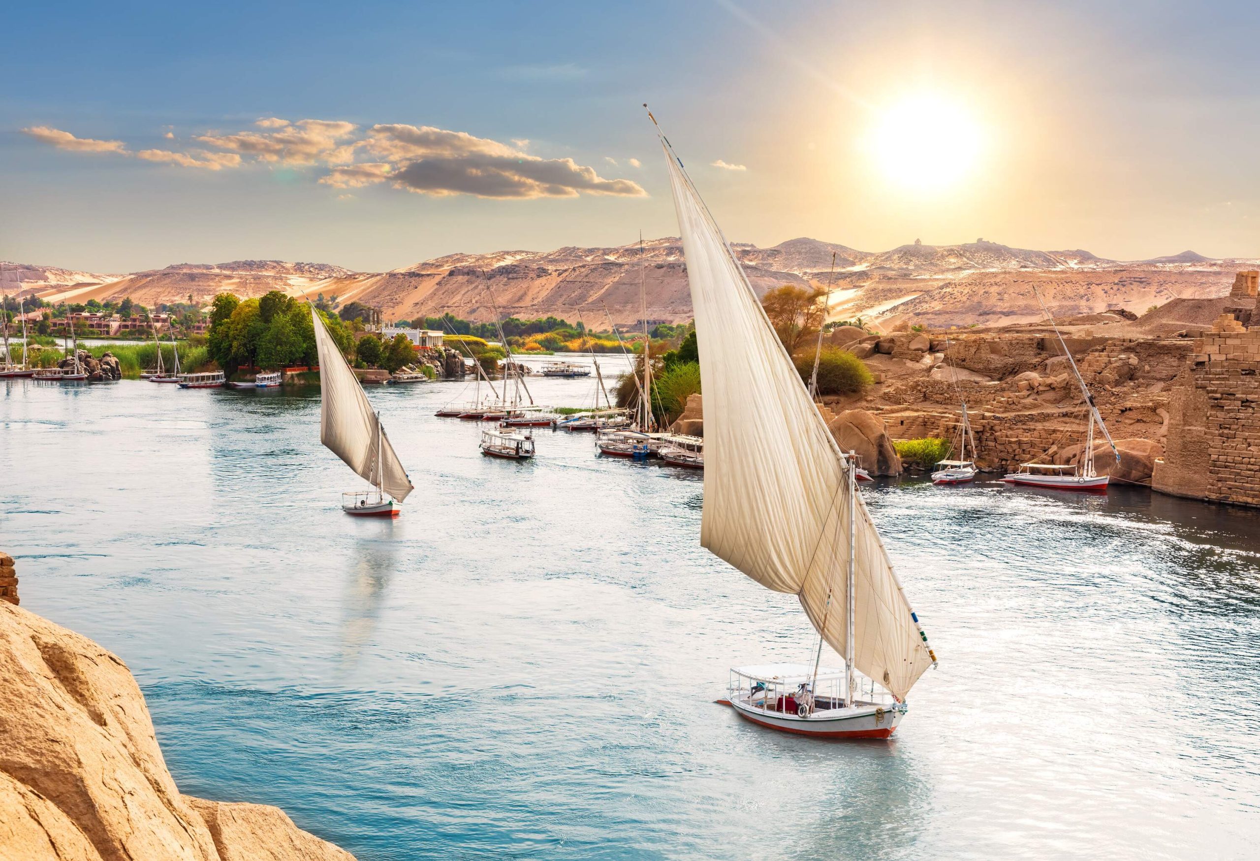 Two sailboats traverse the river, passing by the docked boats along the banks.