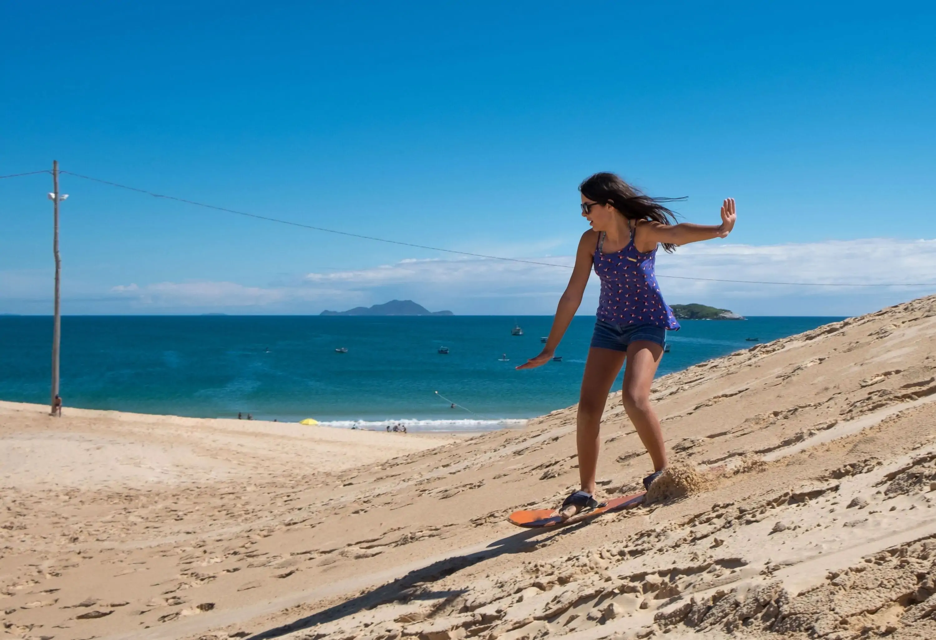 A lady tourist sandboarding on the slope dunes near the sea.