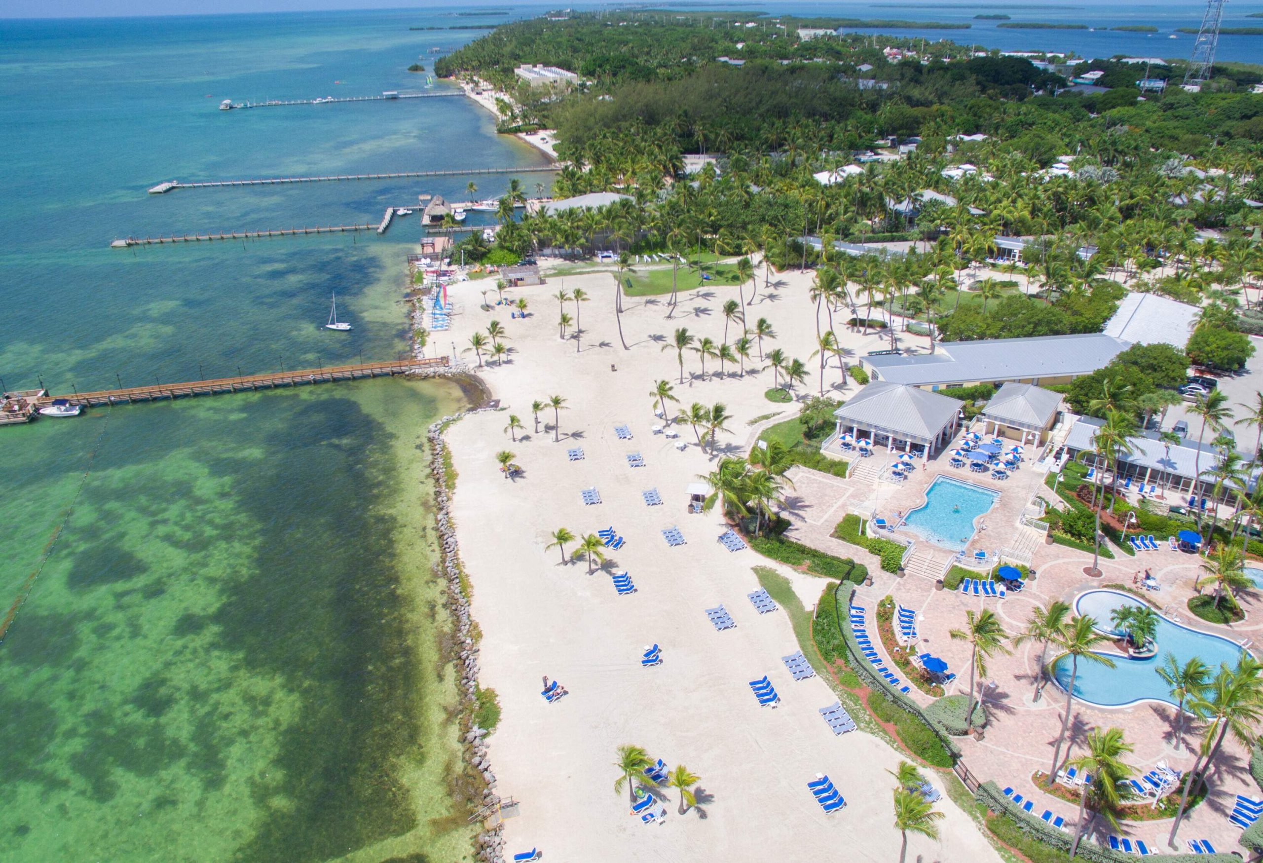 A beach resort with oddly-shaped swimming pools facing a white beach with piers across the sea.