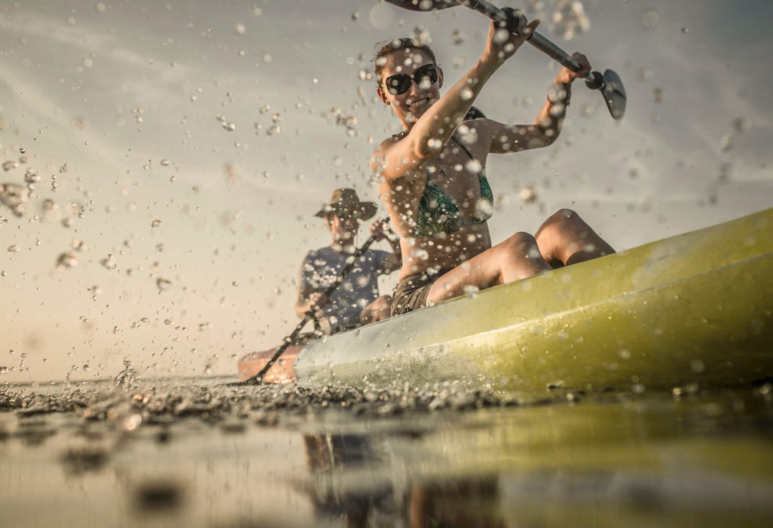 Two people on a canoe paddling across a lake, creating splashes of water.