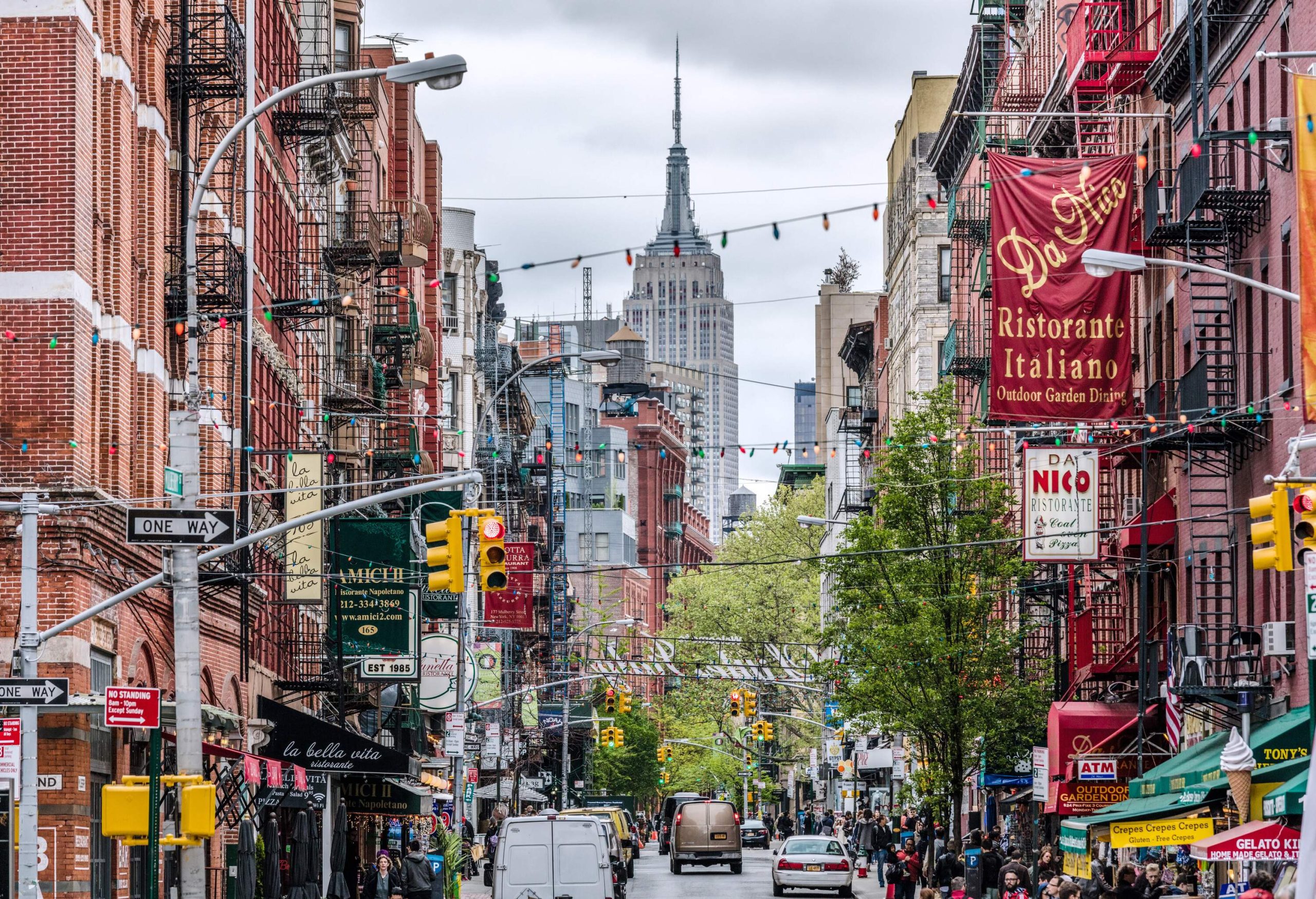 A view of the Empire State Building from a busy street in Little Italy, with buildings on both sides and cars driving past.