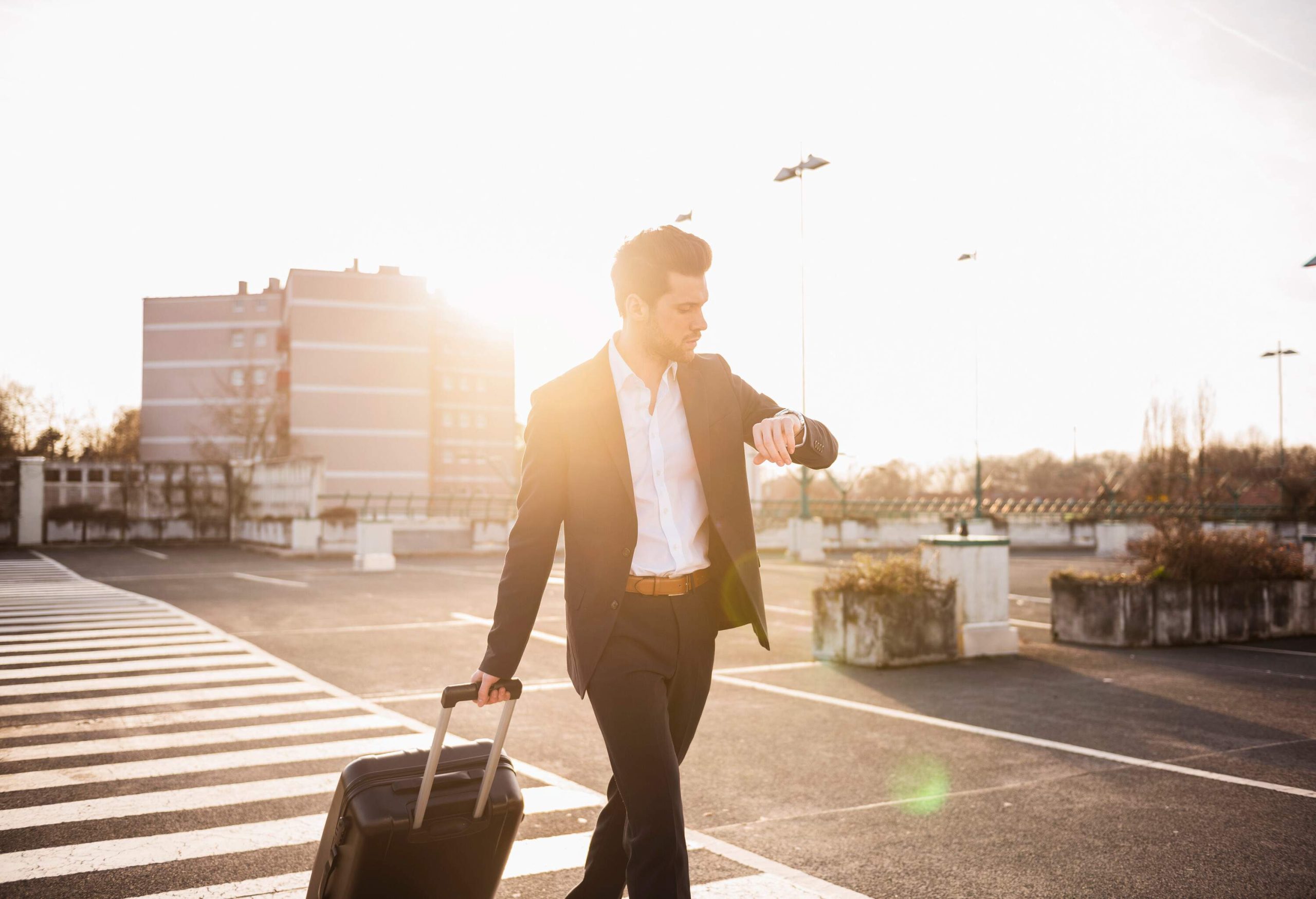 A sharply dressed individual, carrying their luggage, strides purposefully across an empty parking lot.
