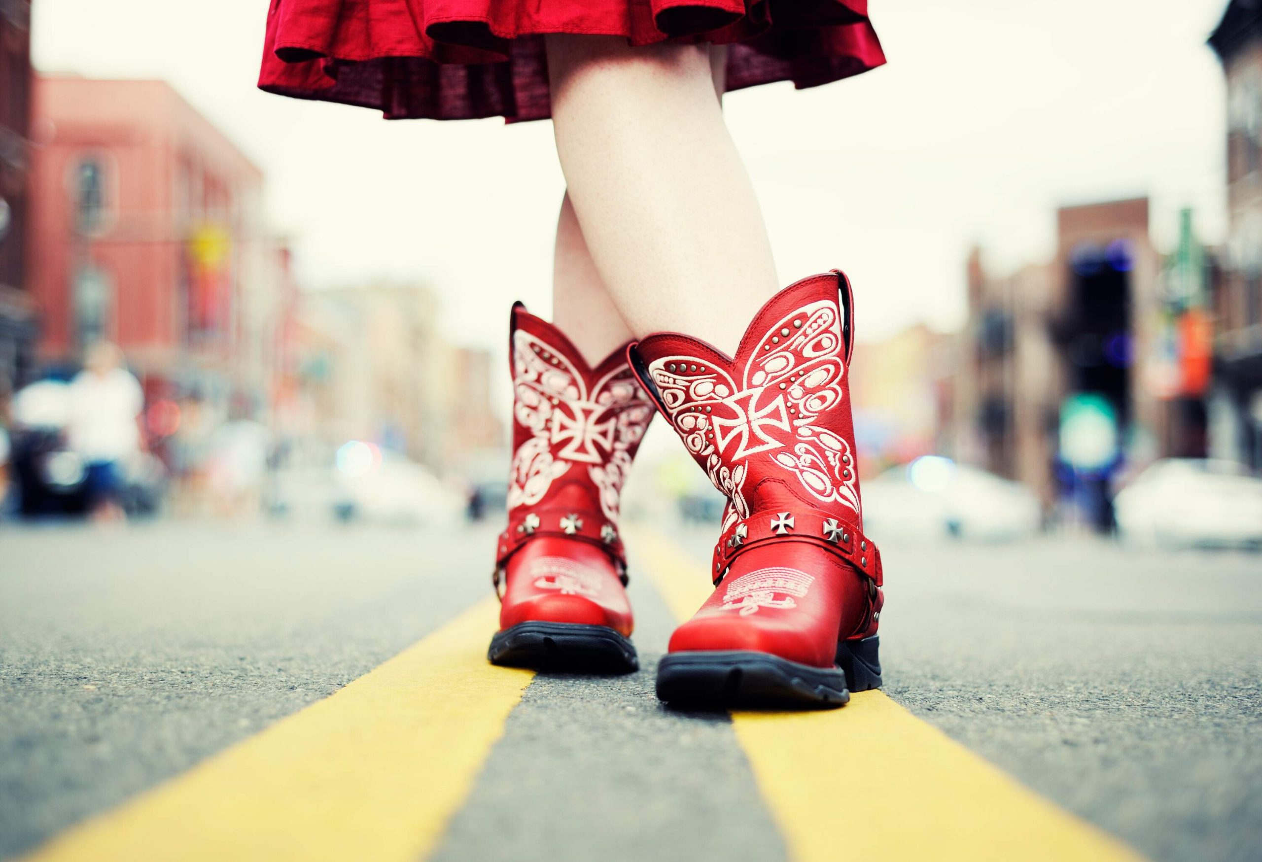 A pair of legs wearing red printed boots standing on two yellow lines in the middle of the road.