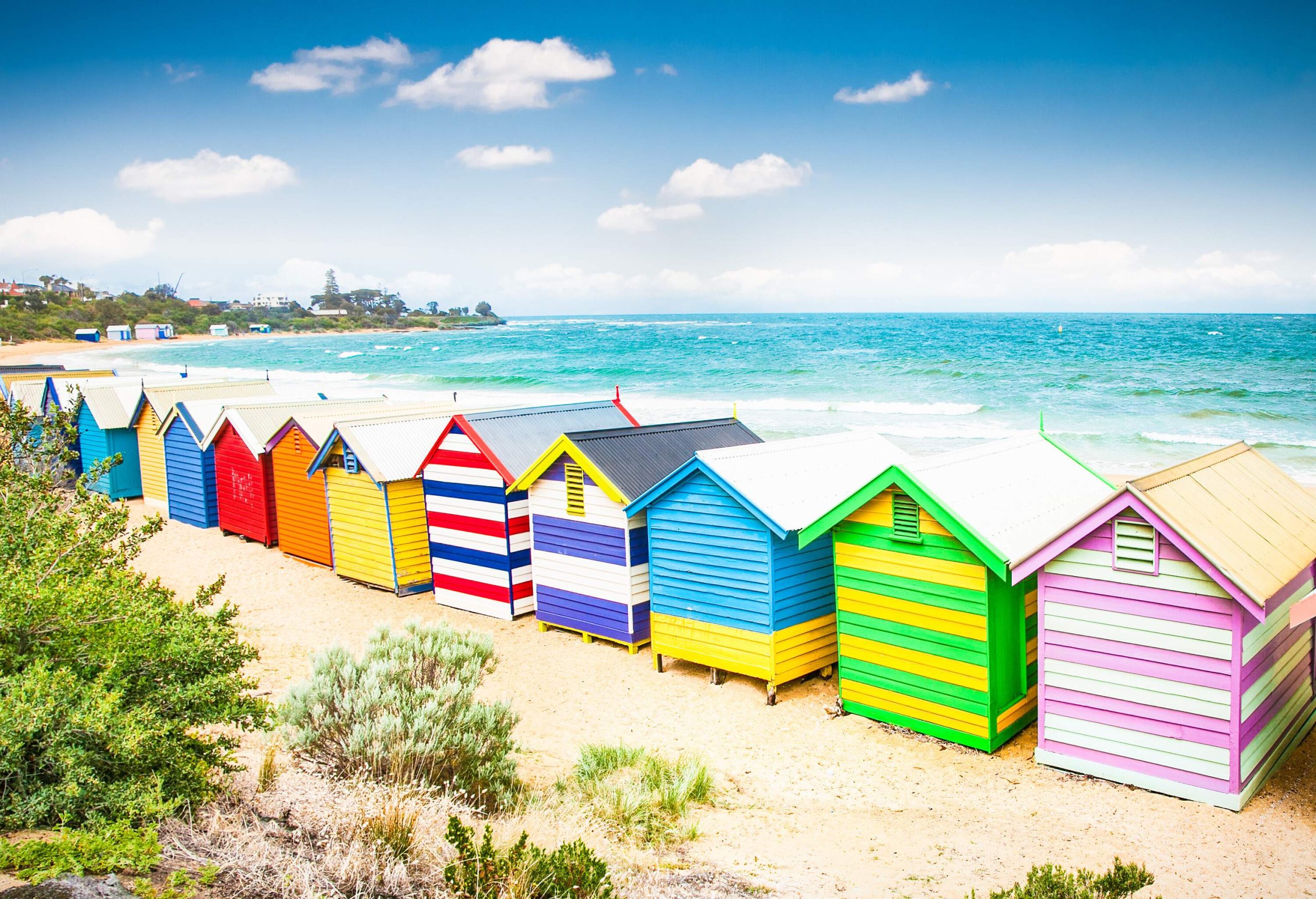 A row of colourful wooden beach huts with vast ocean views.