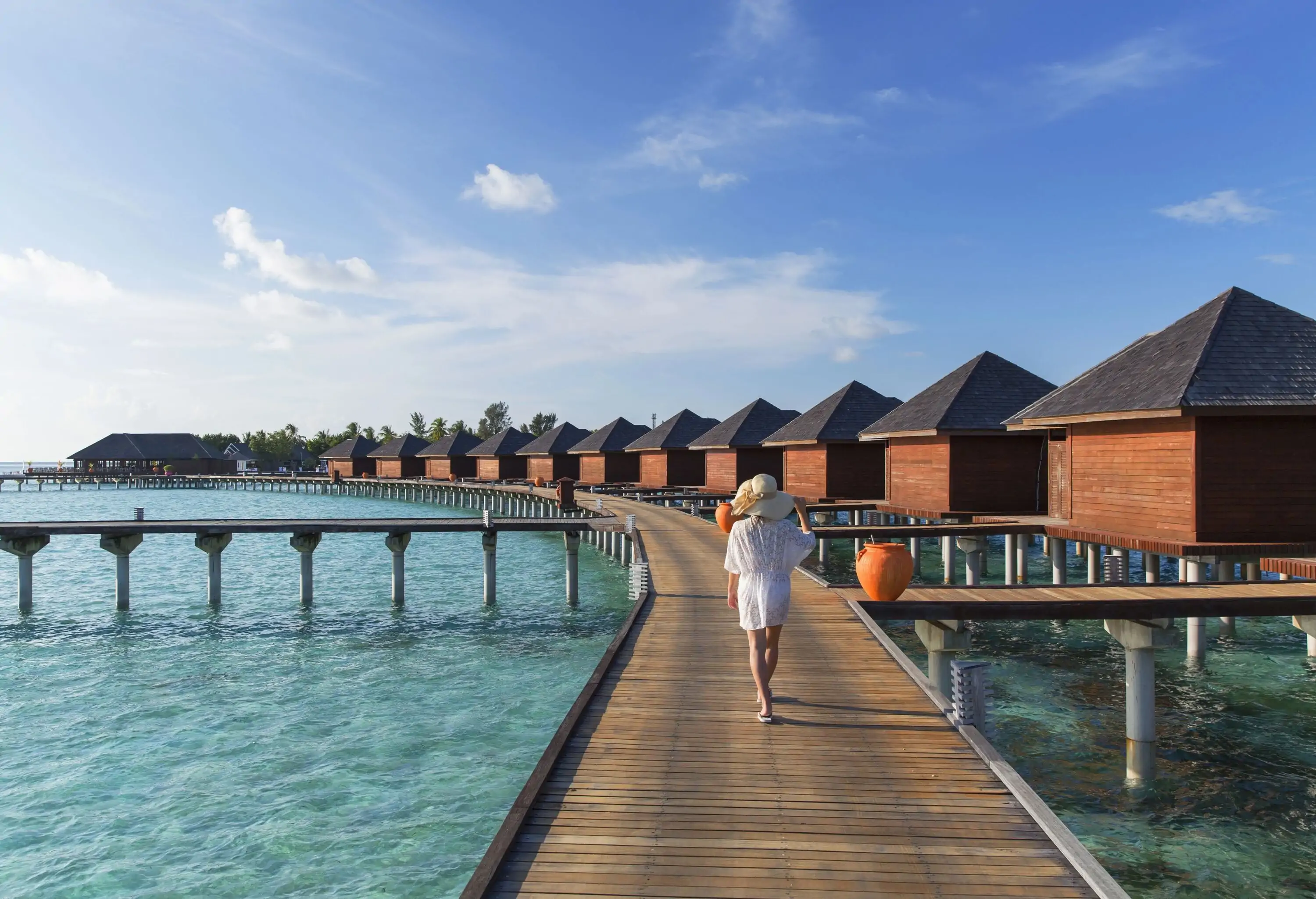 Back view of a lady tourist walking on the boardwalk giving access to the floating villas on the sea.