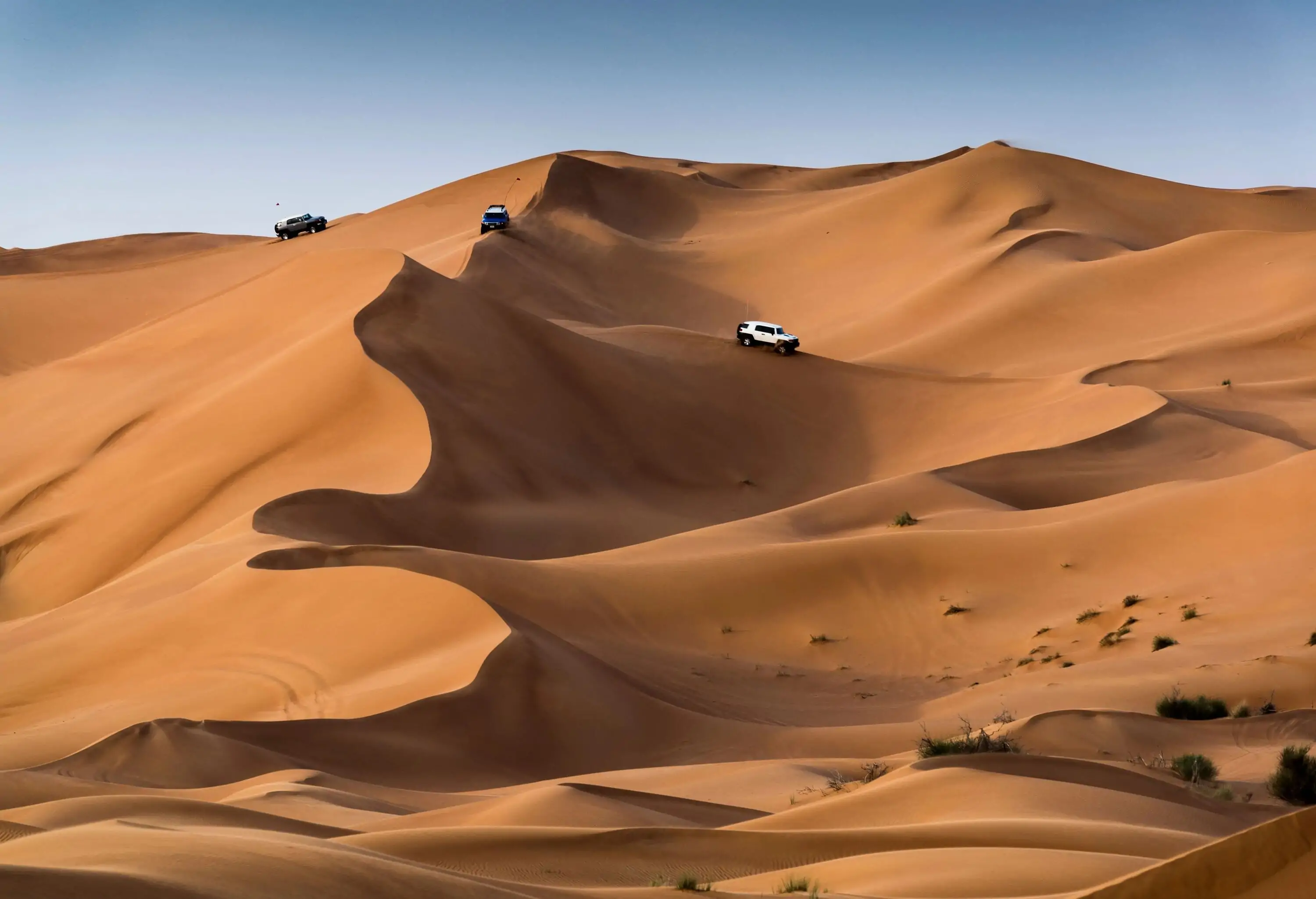 Three SUVs are making their way over the sandy slopes.