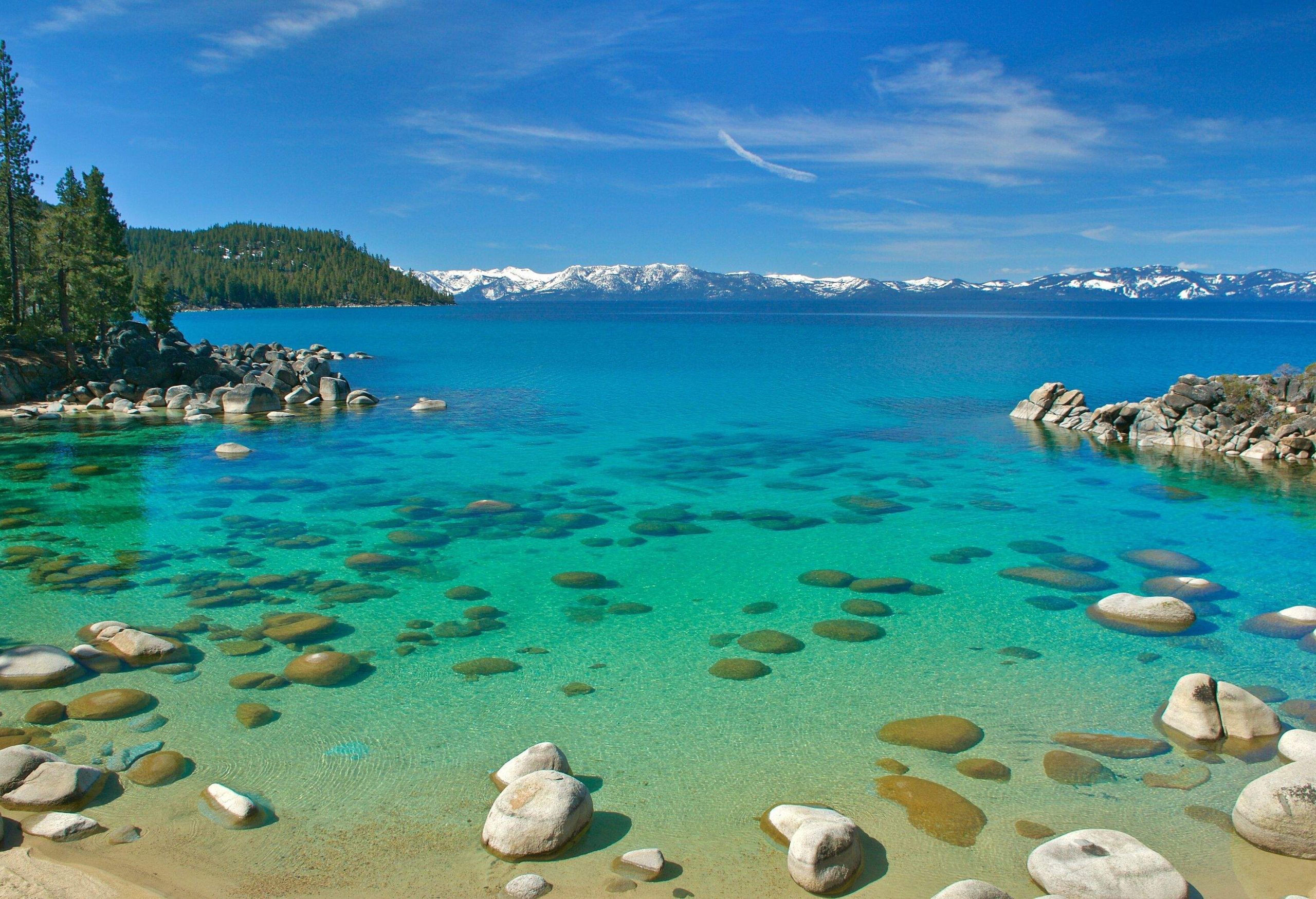 Rocks scattered on the shallow area of a lake with distant views of snowy mountains.