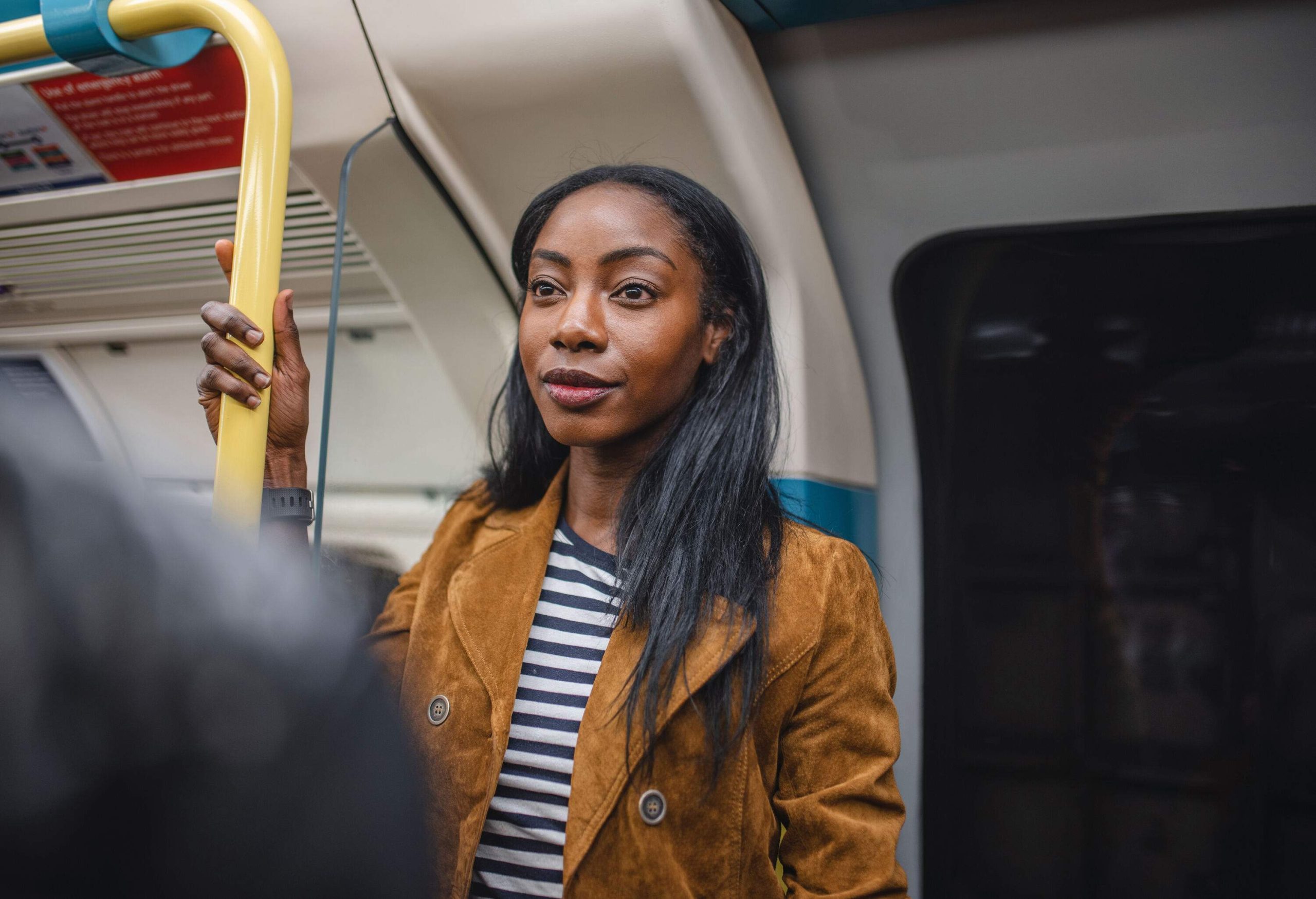 A dark-skinned long hair woman rides the train standing near the door.