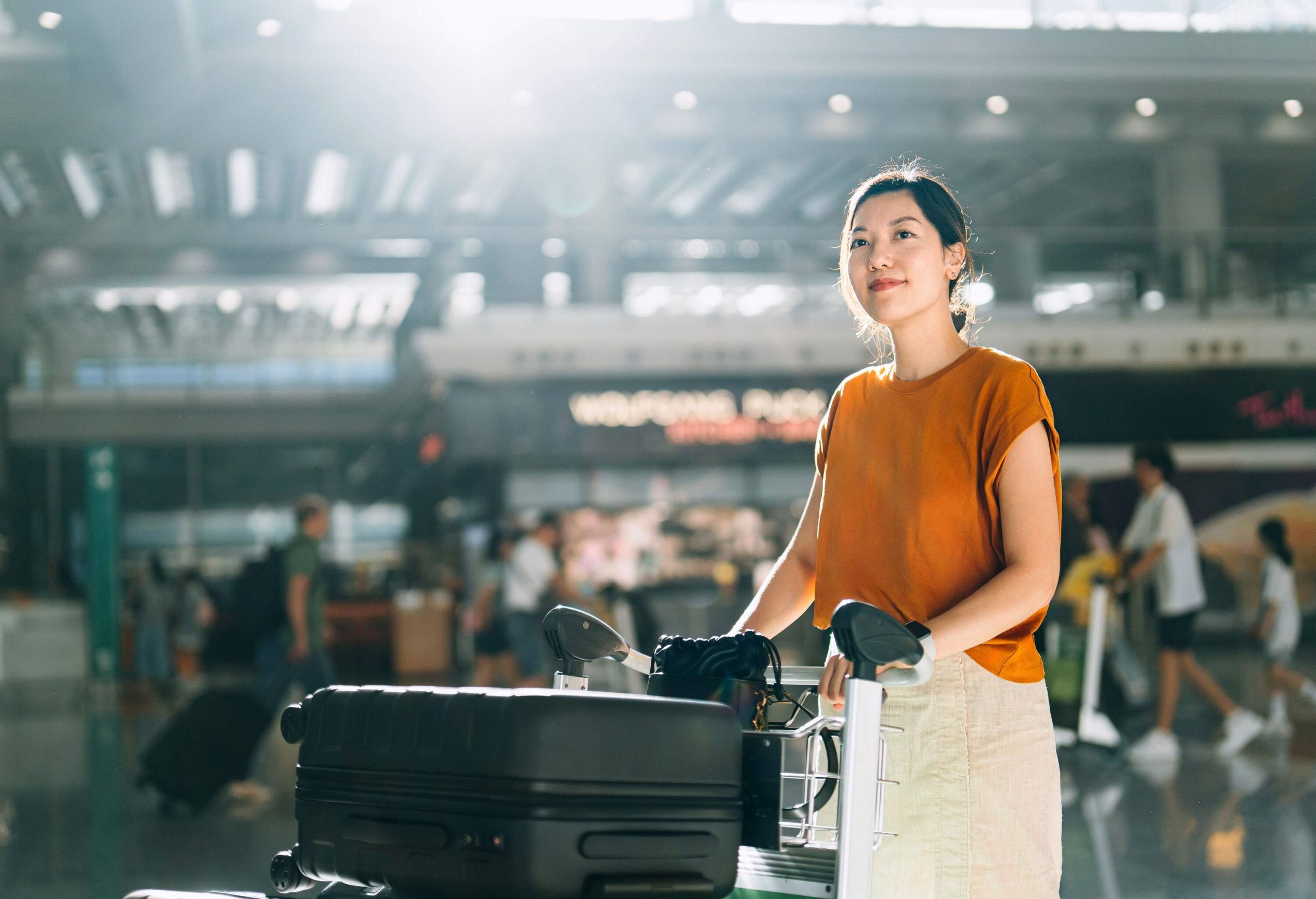 Young Asian woman pushing a luggage trolley with suitcases to the check-in counter at airport terminal. Ready for a trip. Business travel. Travel and vacation concept