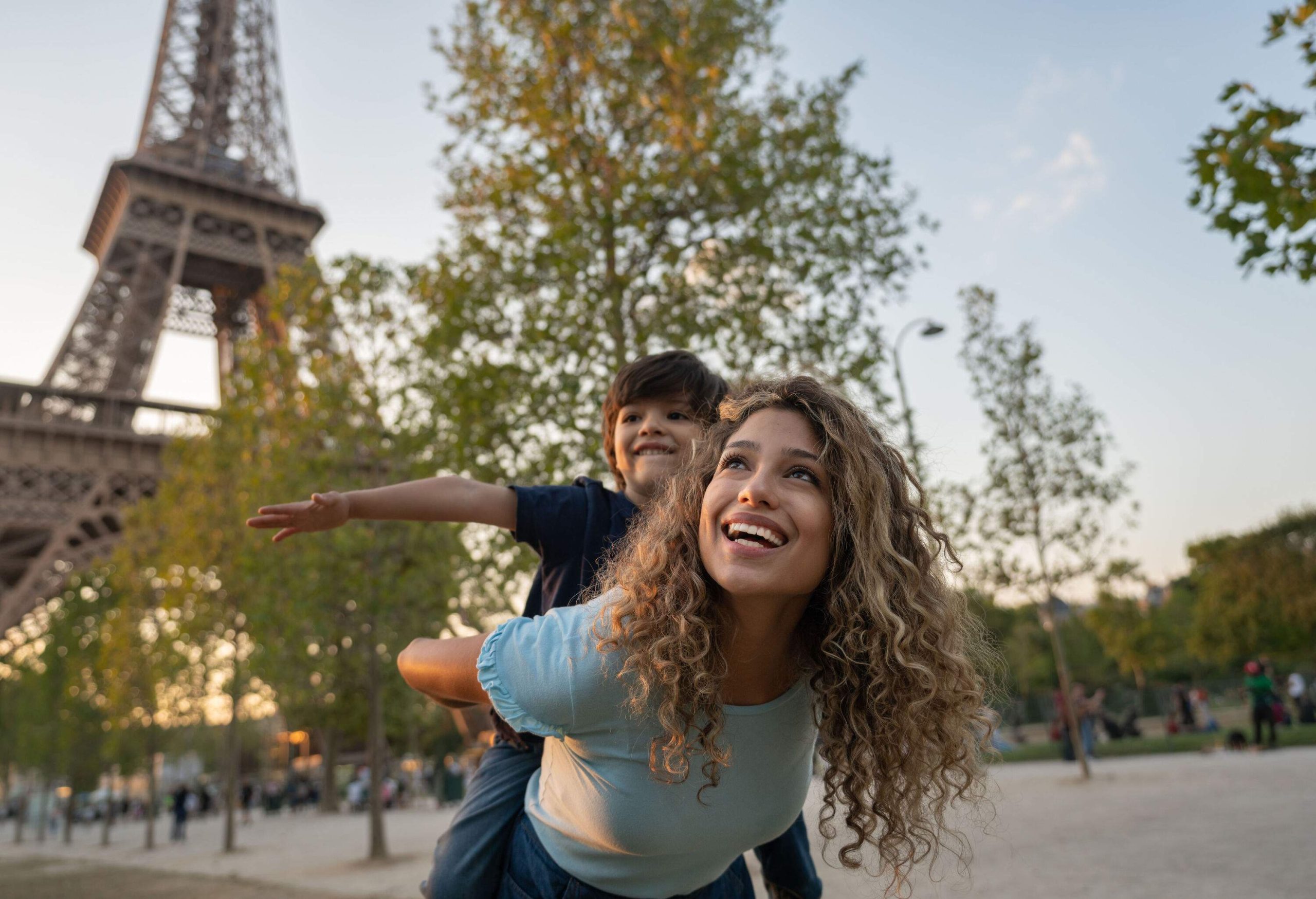 A happy mother with her son on her back in the park near the Eiffel Tower.