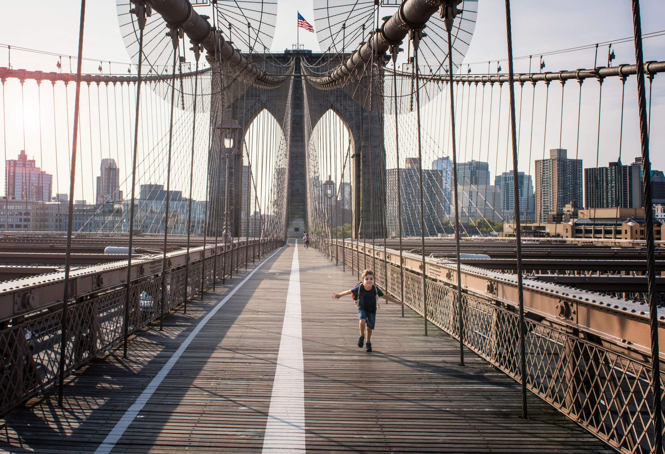 A boy runs across a footbridge with distant views of the city skyline.