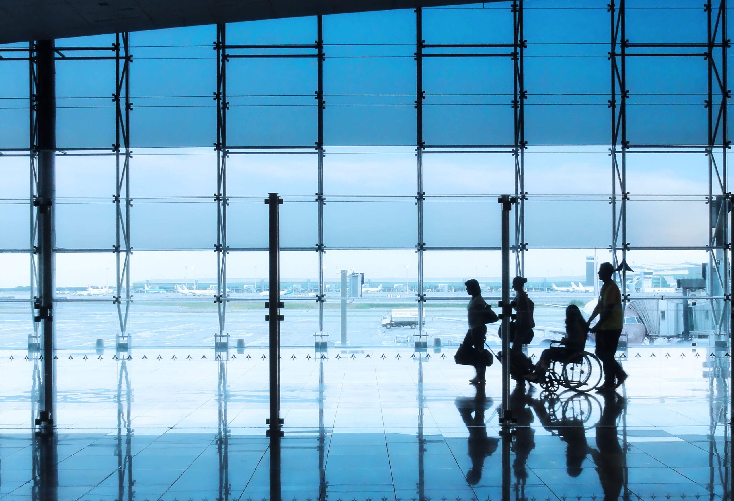 A silhouette of four people, one of them using a wheelchair, walking through the airport.
