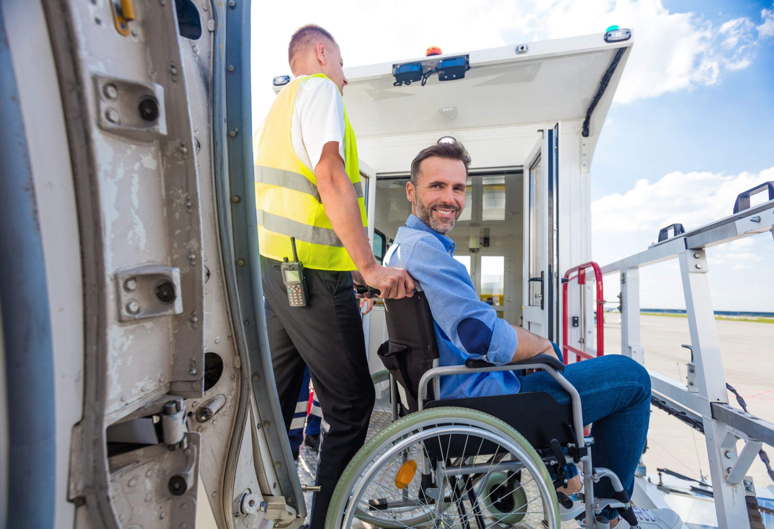 Ground service men helping wheelchair passenger to enter on airplane board, they using an elevator. Disabled man smiling at camera.