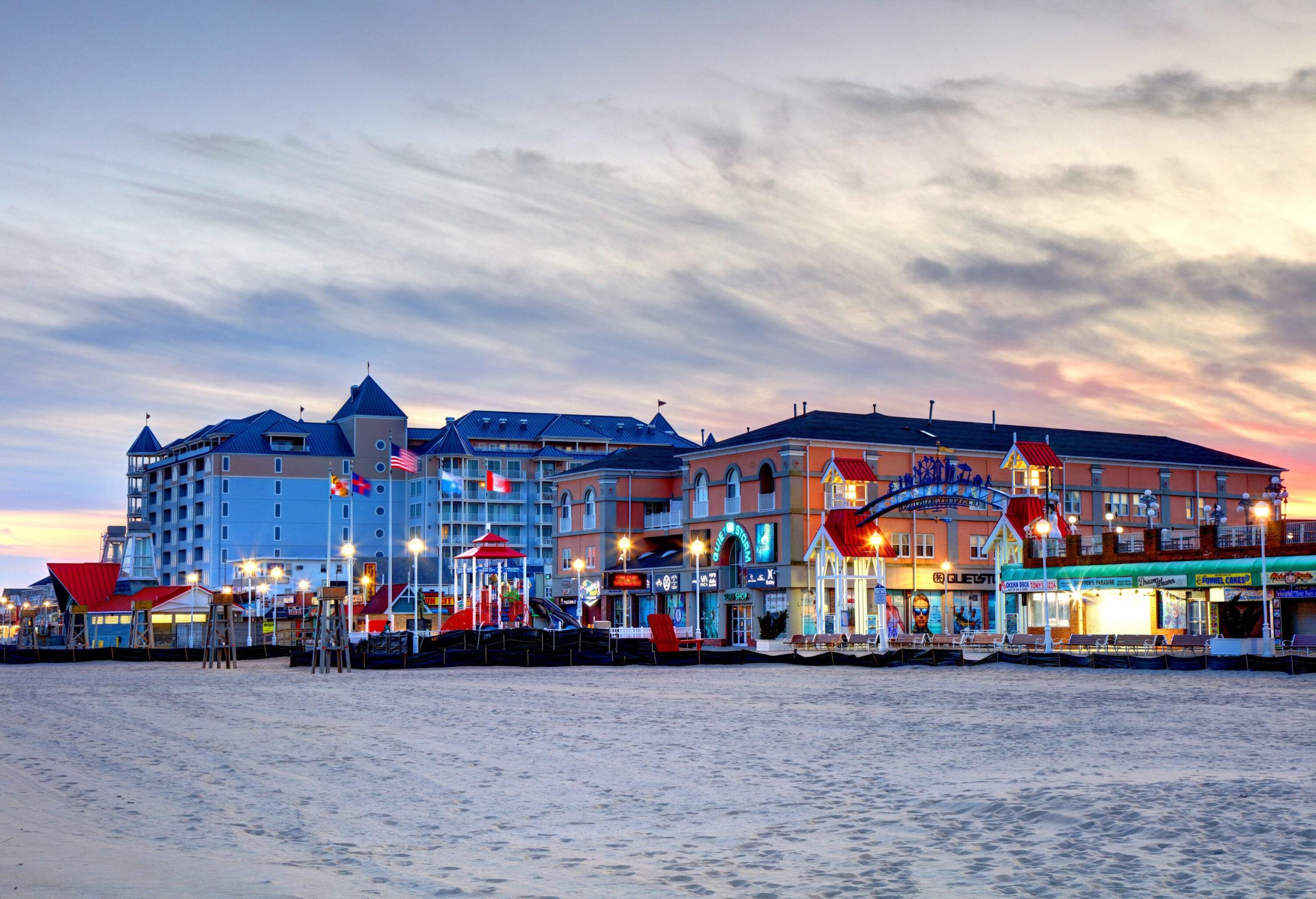 A recreational pier on the beach with national flags flying in front of red and blue buildings.