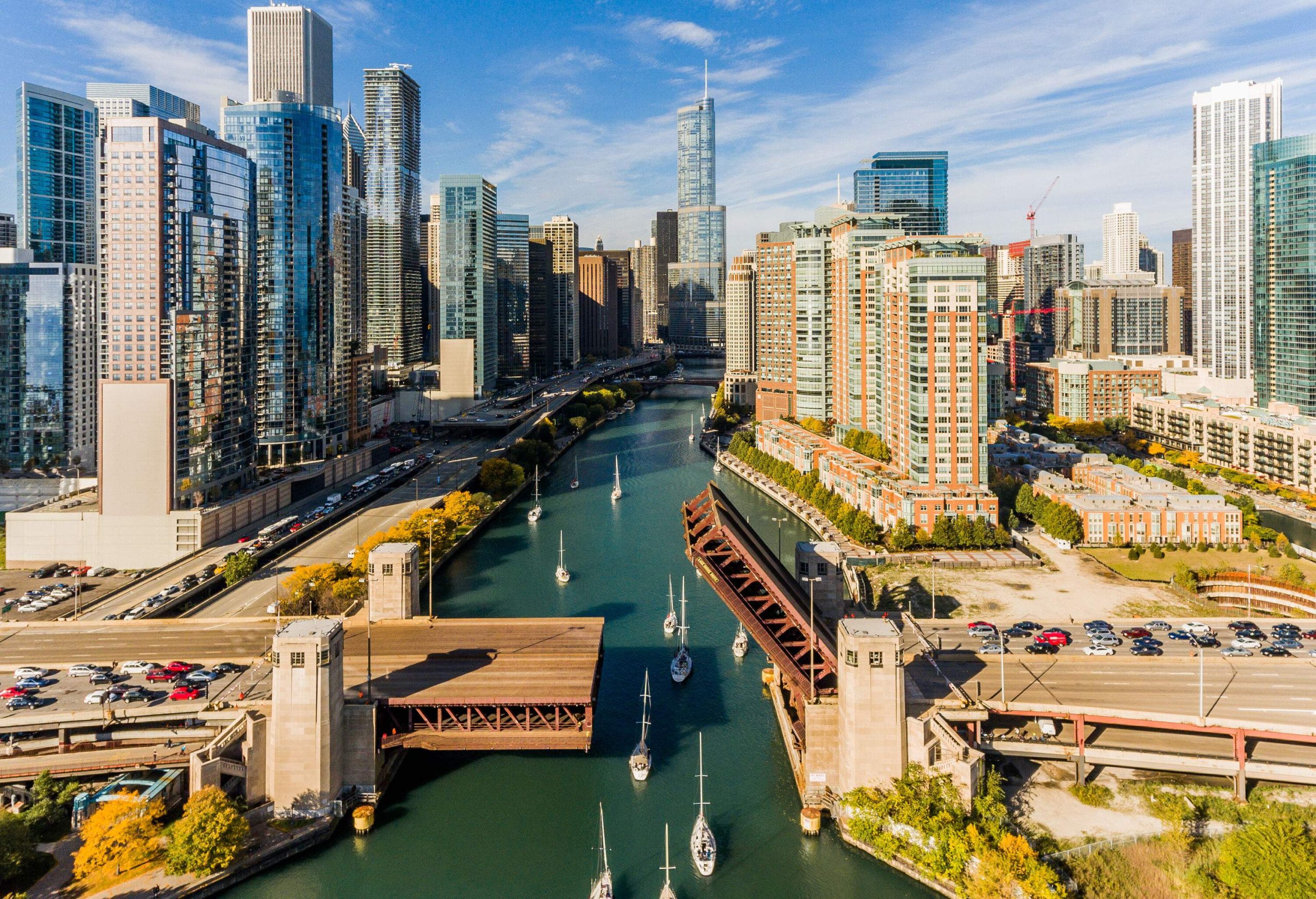 Aerial view of boats on a river surrounded by modern and towering skyscrapers.