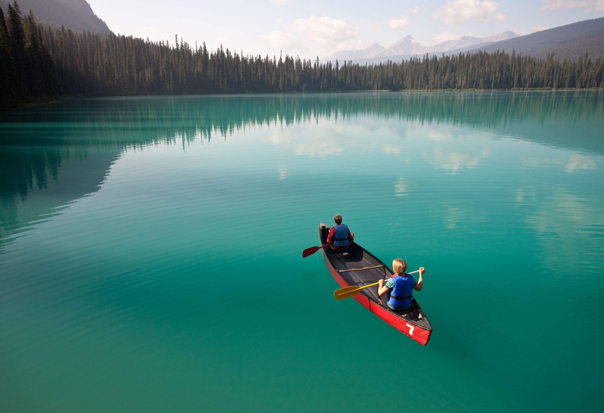 Two people on a canoe floating on a calm lake surrounded by a forest.