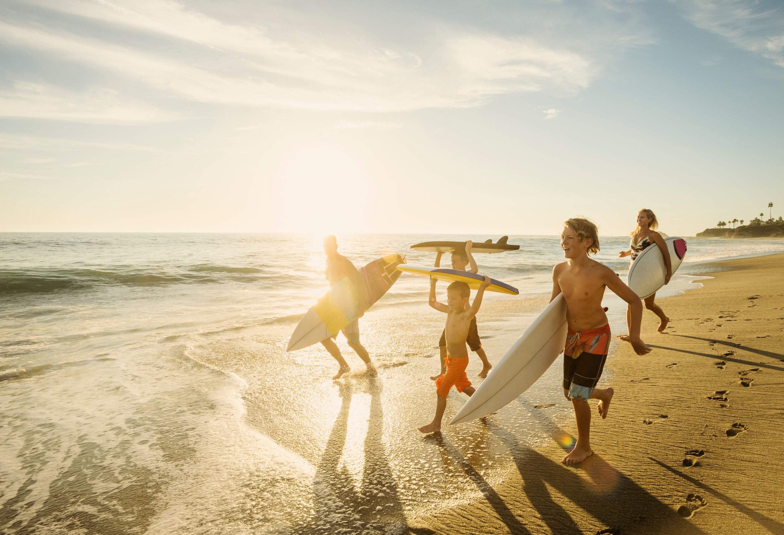 Family of surfers carrying surfboards along the beach