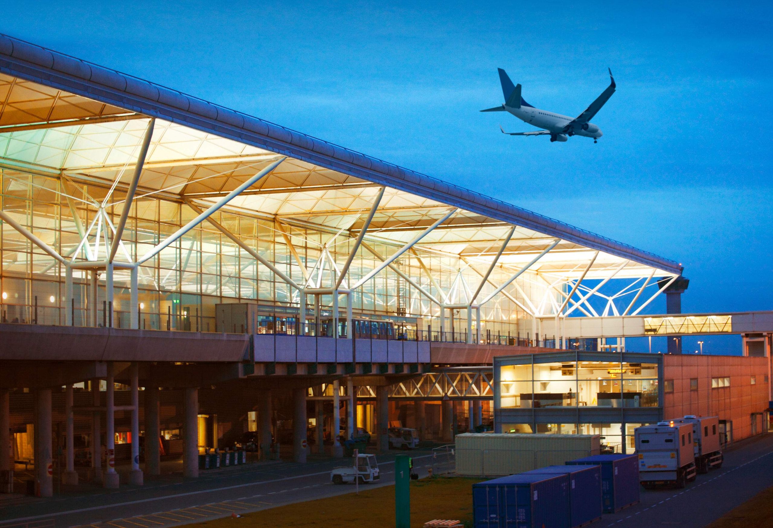 An aircraft flying above an airport terminal.