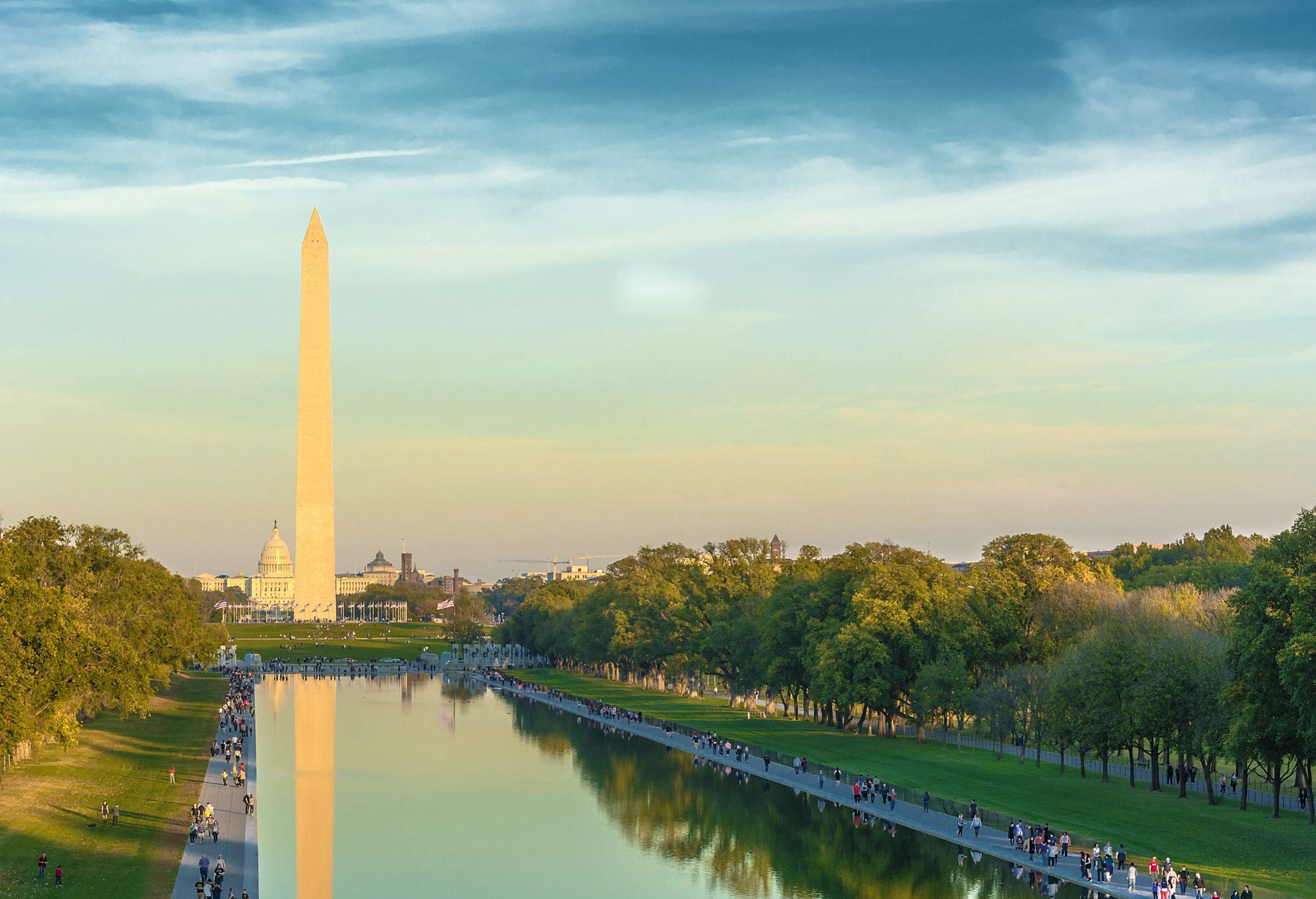 The Washington Monument and the Capitol Building may be seen in the backdrop as people meander around the Tidal Basin.