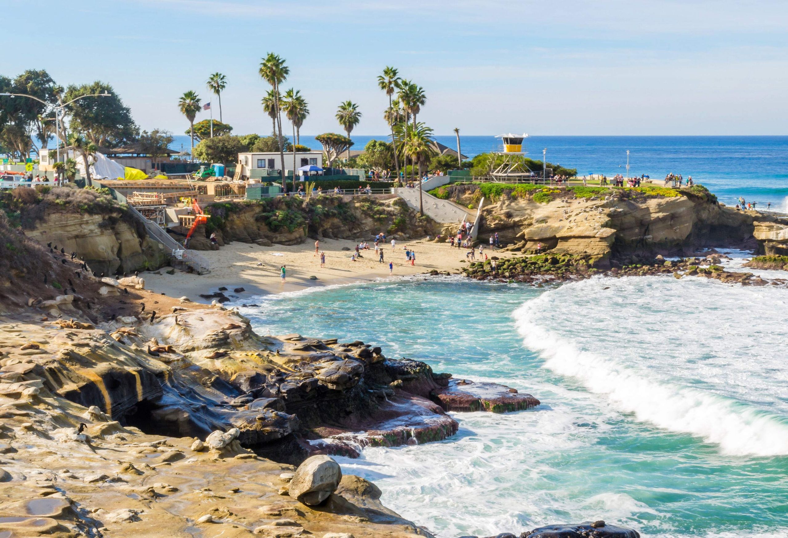 A hidden beach nestled amidst rugged coasts unveils its serene beauty, with buildings peeking through the landscape and swaying palms.