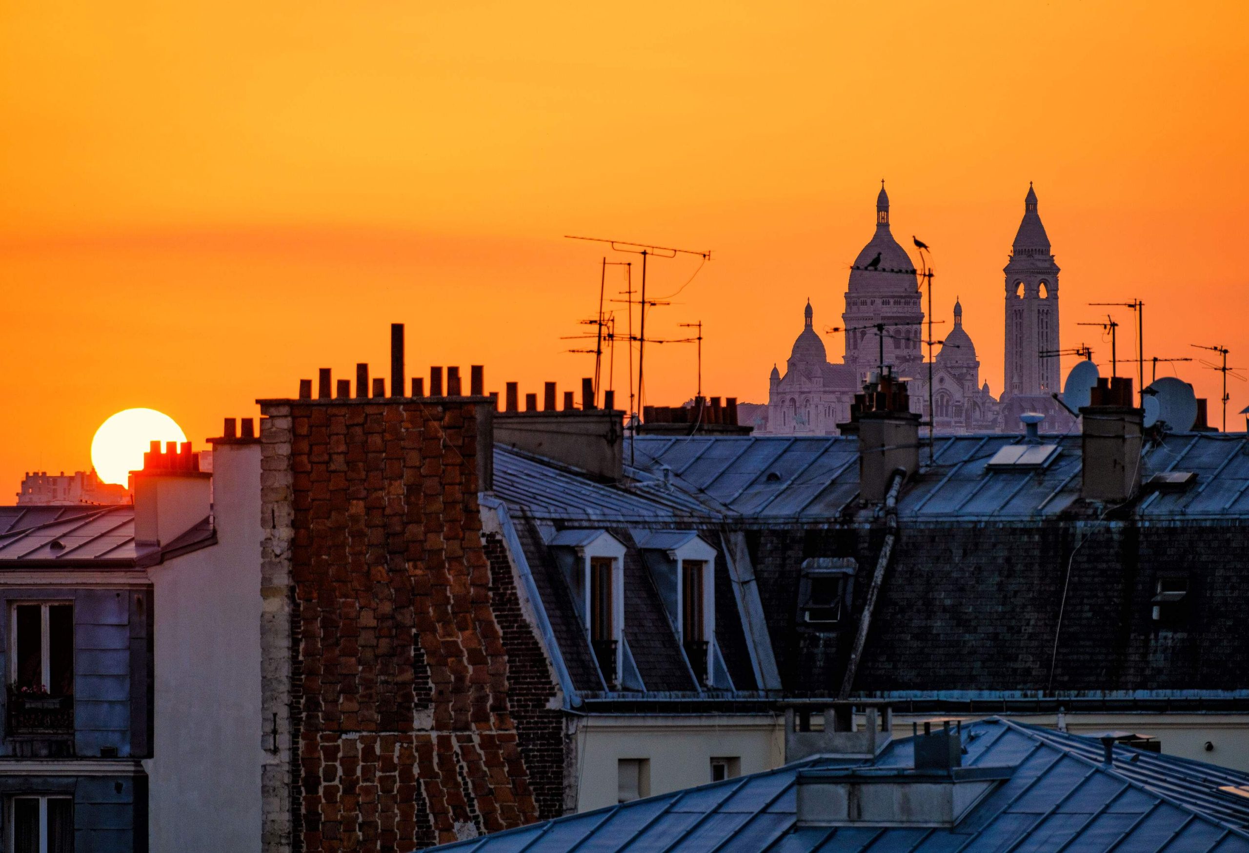 Iconic bell towers and building rooftops set against a yellow orange sunset sky.