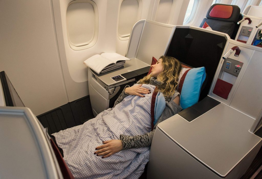 A woman comfortably sleeps on a reclined airplane seat.